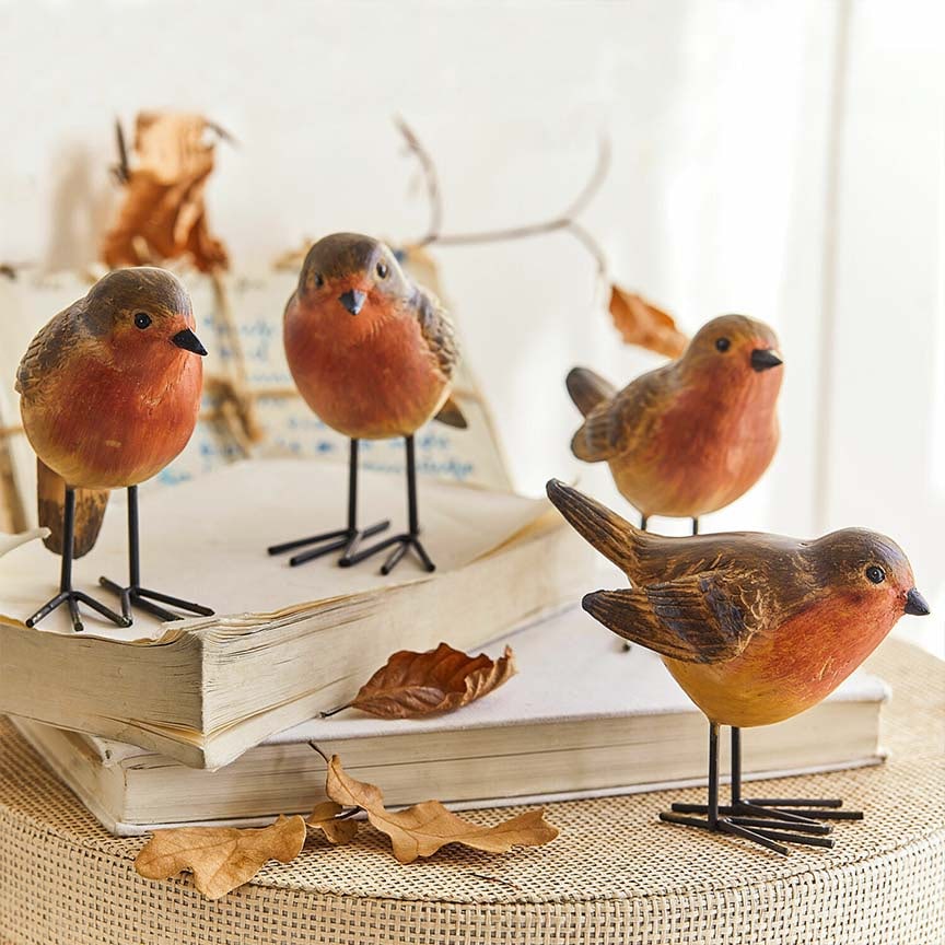 Dekorative Vogel-Figuren aus Holz in warmen Orange- und Brauntönen auf Büchern mit trockenen Blättern