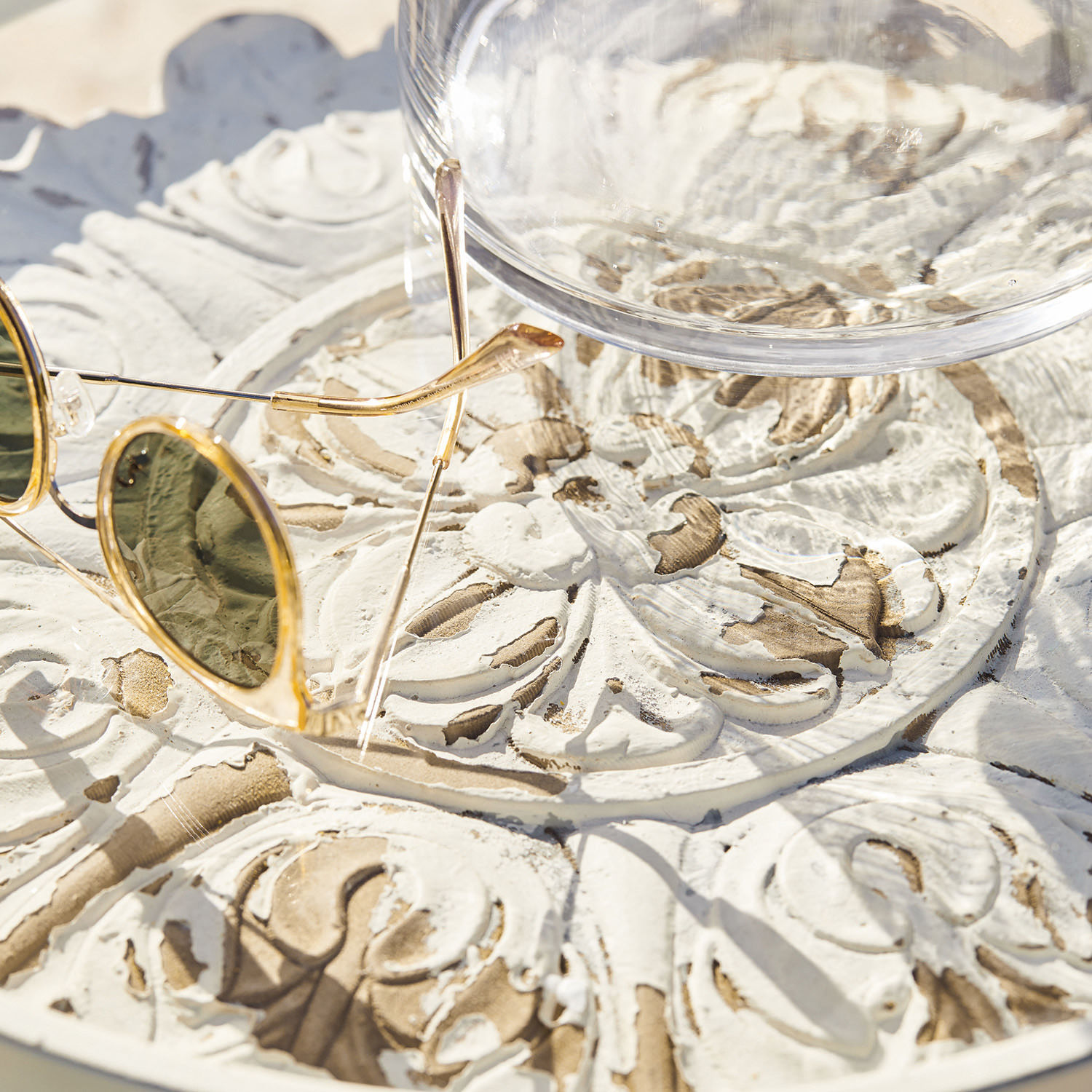Weiß lackierte Holzplatte mit geschnitztem Muster, Sonnenbrille und Glas darauf