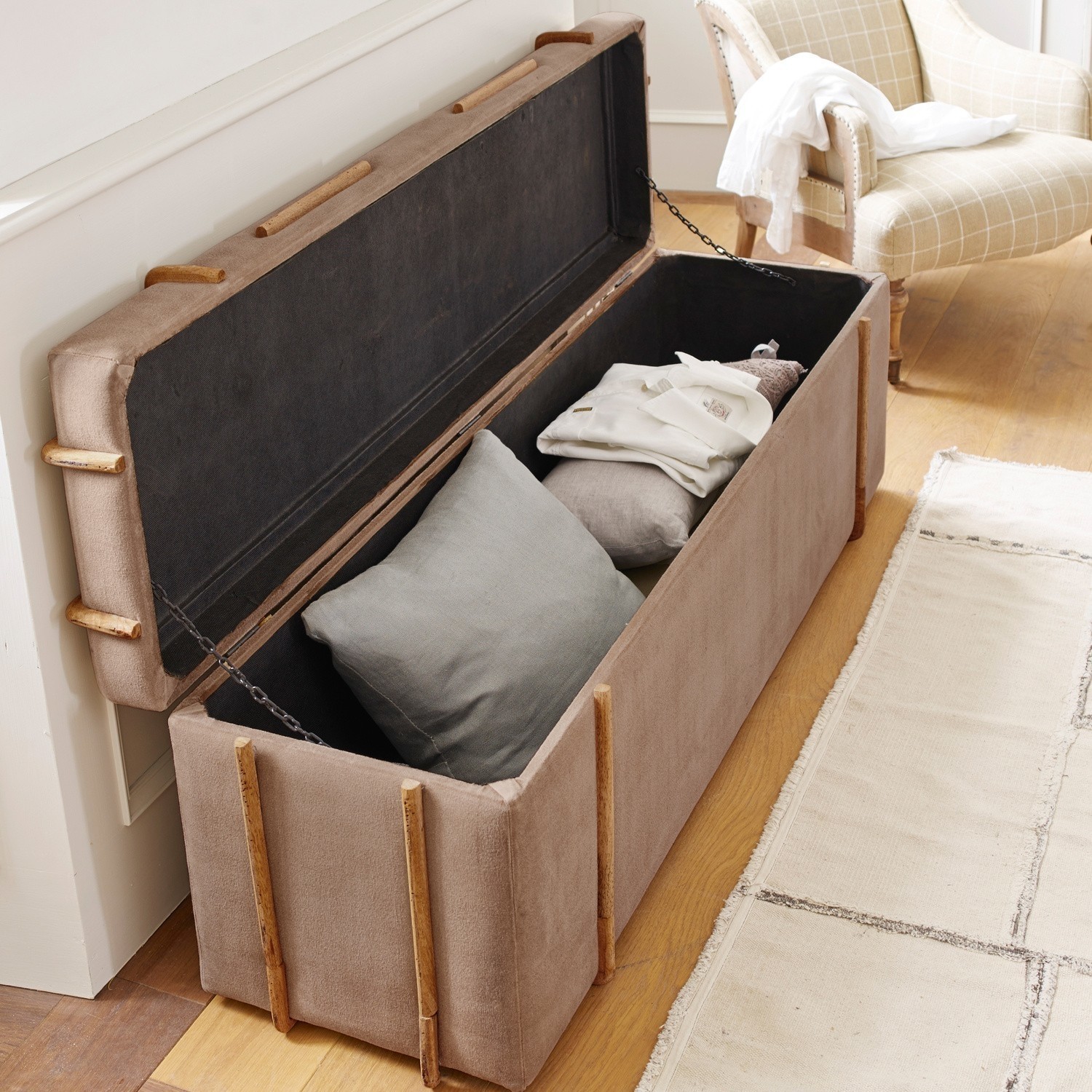 Beige Stofftruhe mit Holzdetails, offen mit Kissen und Kleidung, Stauraum im Wohnzimmer
