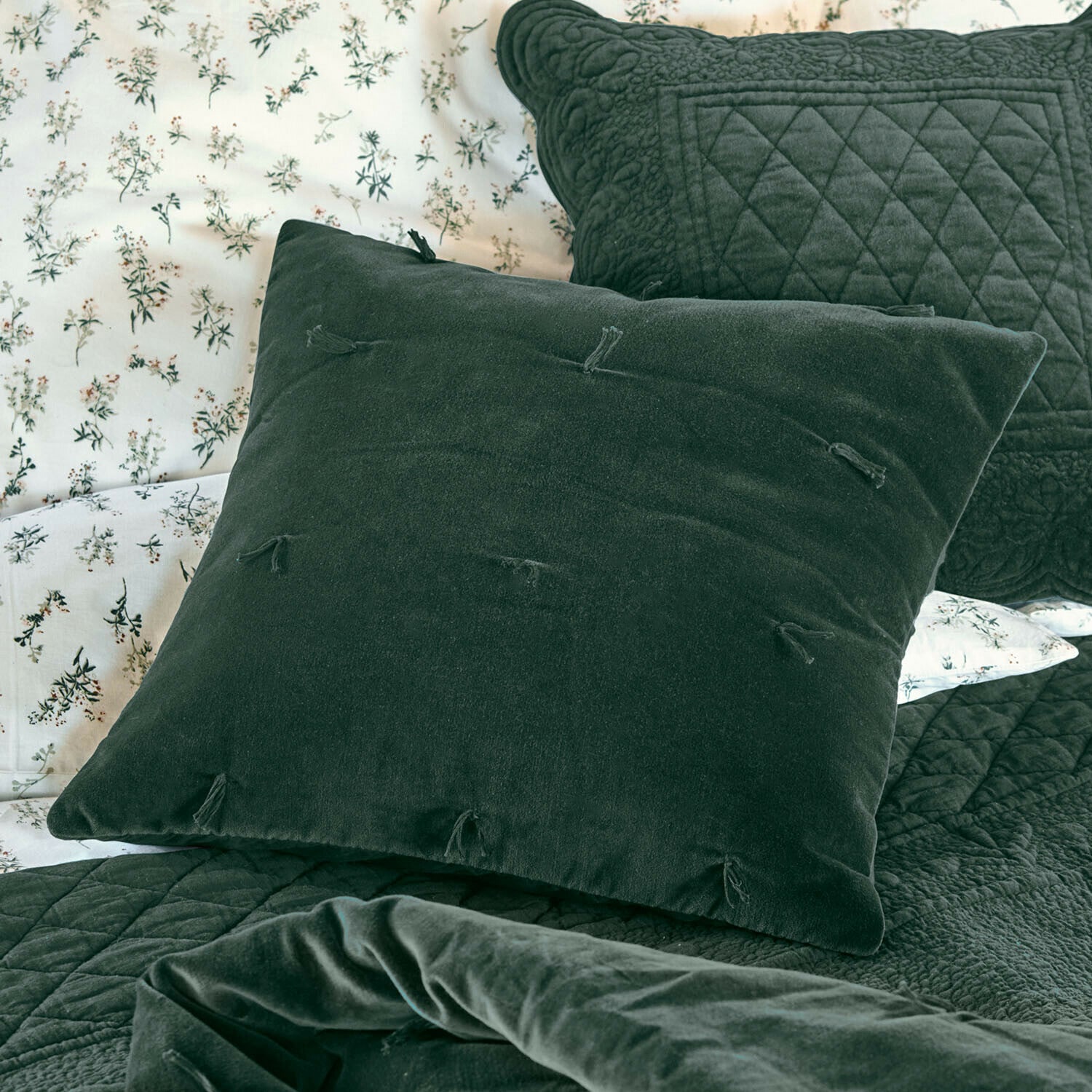 Kissenhülle Orélisse Grünes Samtkissen mit Quasten auf Bett mit gesteppter Decke und floralem Bettbezug