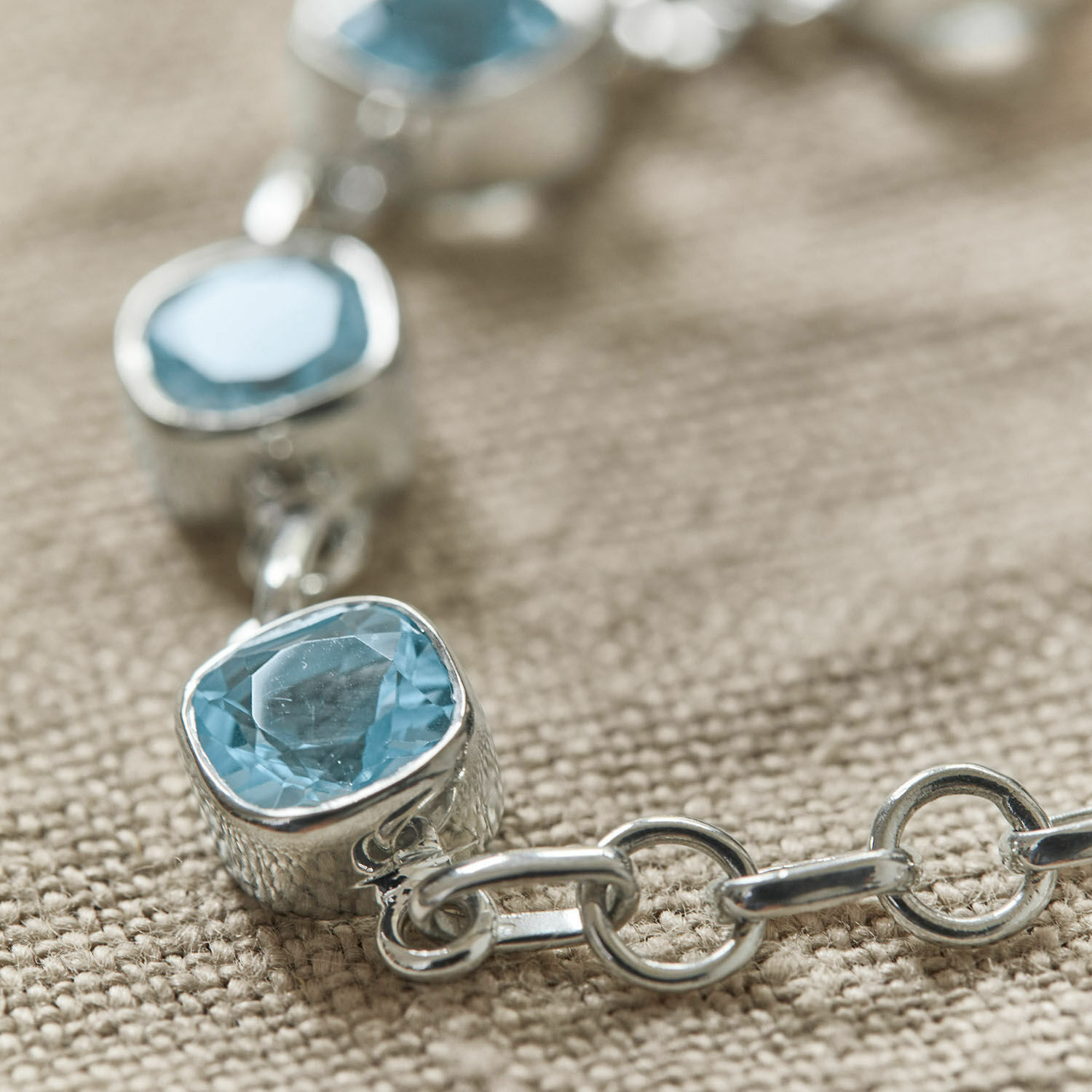 Armband mit blauen Steinen und silberner Kette auf beigem Hintergrund, Damenschmuck