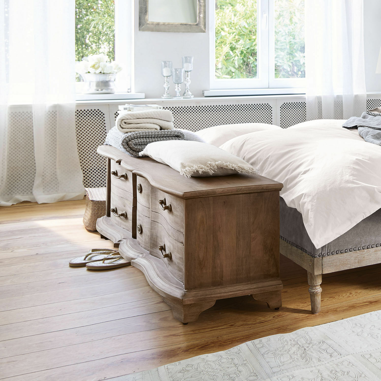 Holzkommode mit wellenförmigen Fronten und Messinggriffen in hellem Schlafzimmer mit Tageslicht