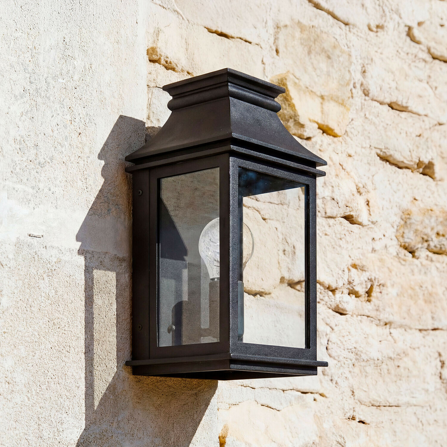 Schwarze Metall-Wandleuchte mit klarem Glas an heller Steinwand, klassische Außenbeleuchtung