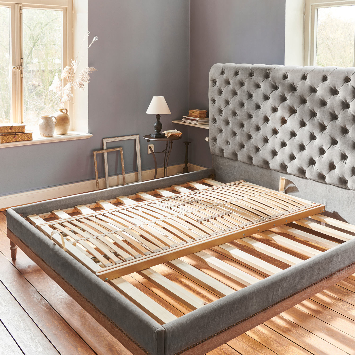 Grau gepolstertes Bett mit gestepptem Kopfteil und Holzlattenrost in hellem Schlafzimmer