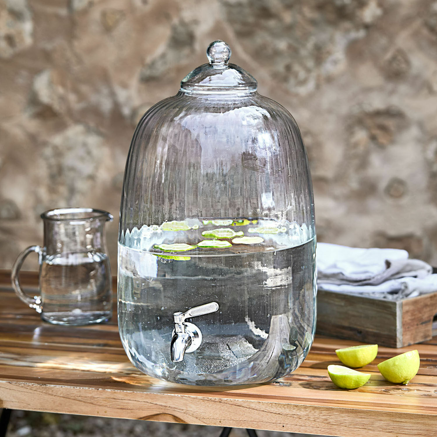 Getränkespender Alindor Glas-Wasserspender mit Zapfhahn und Deckel, durchsichtig, mit Limettenscheiben auf Holztisch
