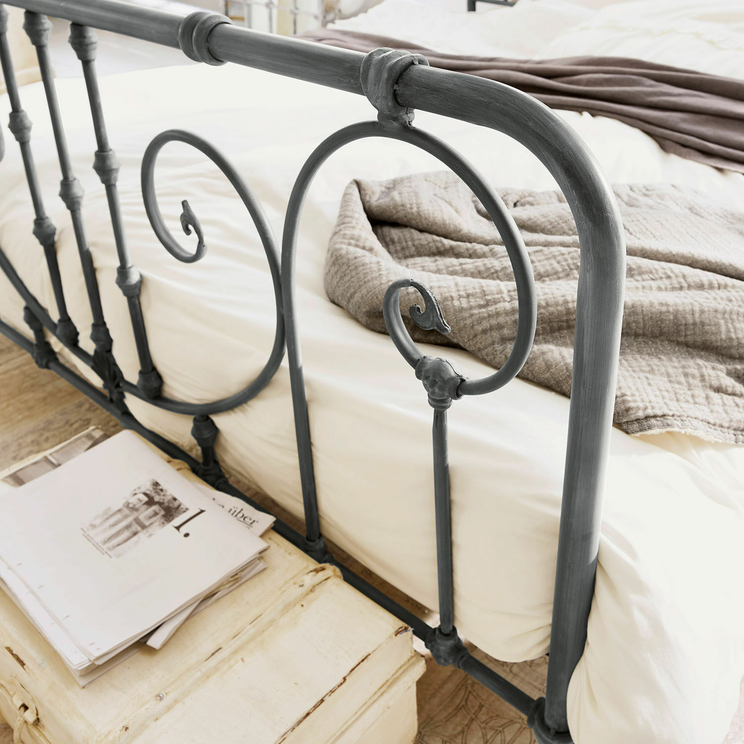 Graues Metallbett mit dekorativem Kopfteil und beiger Bettwäsche im Schlafzimmer