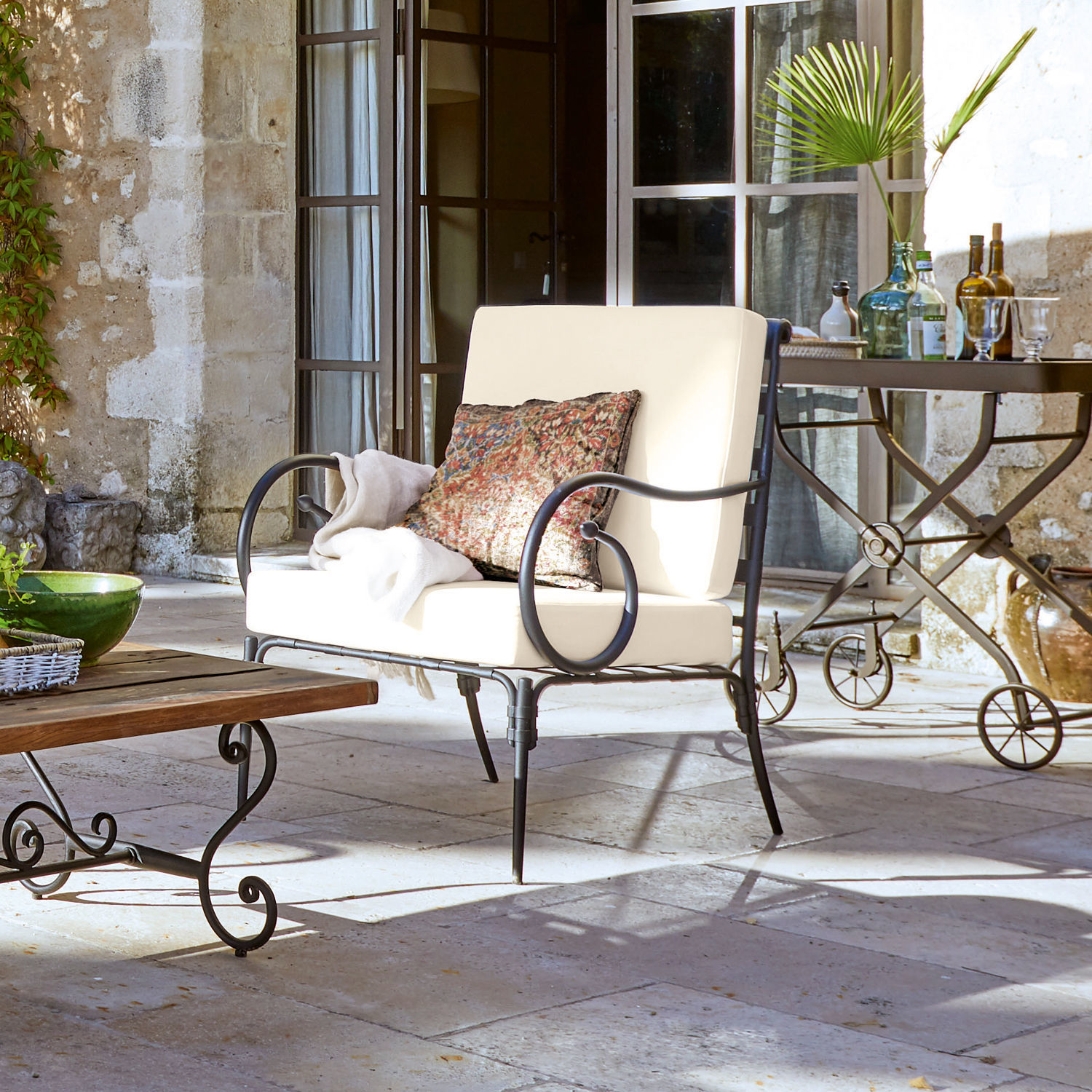 Sessel Neret Metall-Gartensofa mit cremefarbenen Polstern und dekorativem Kissen auf Steinpatio