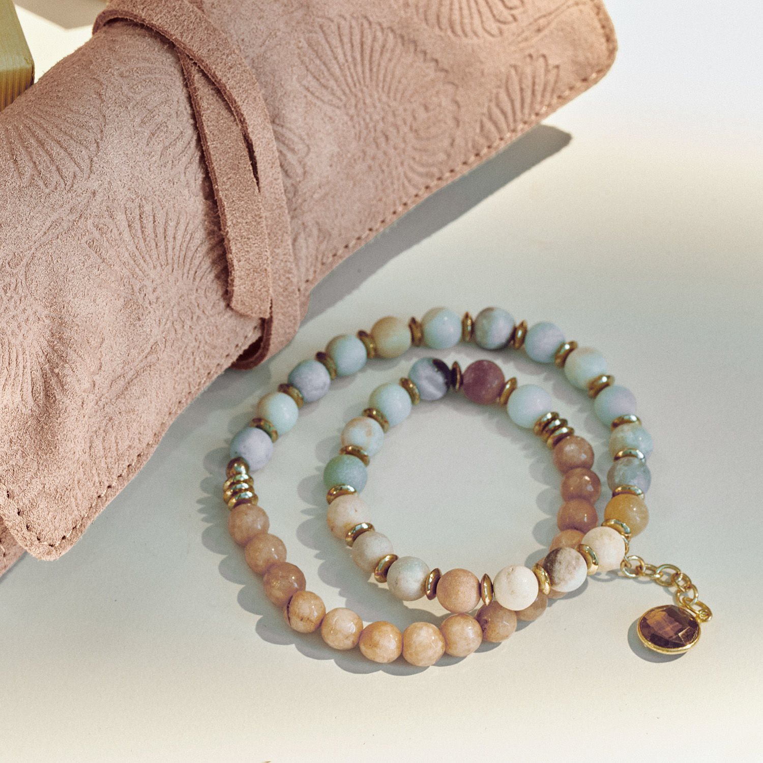 Armbänder aus Natursteinen in Pastellfarben mit goldenen Details und beigem Wildlederetui mit Muster