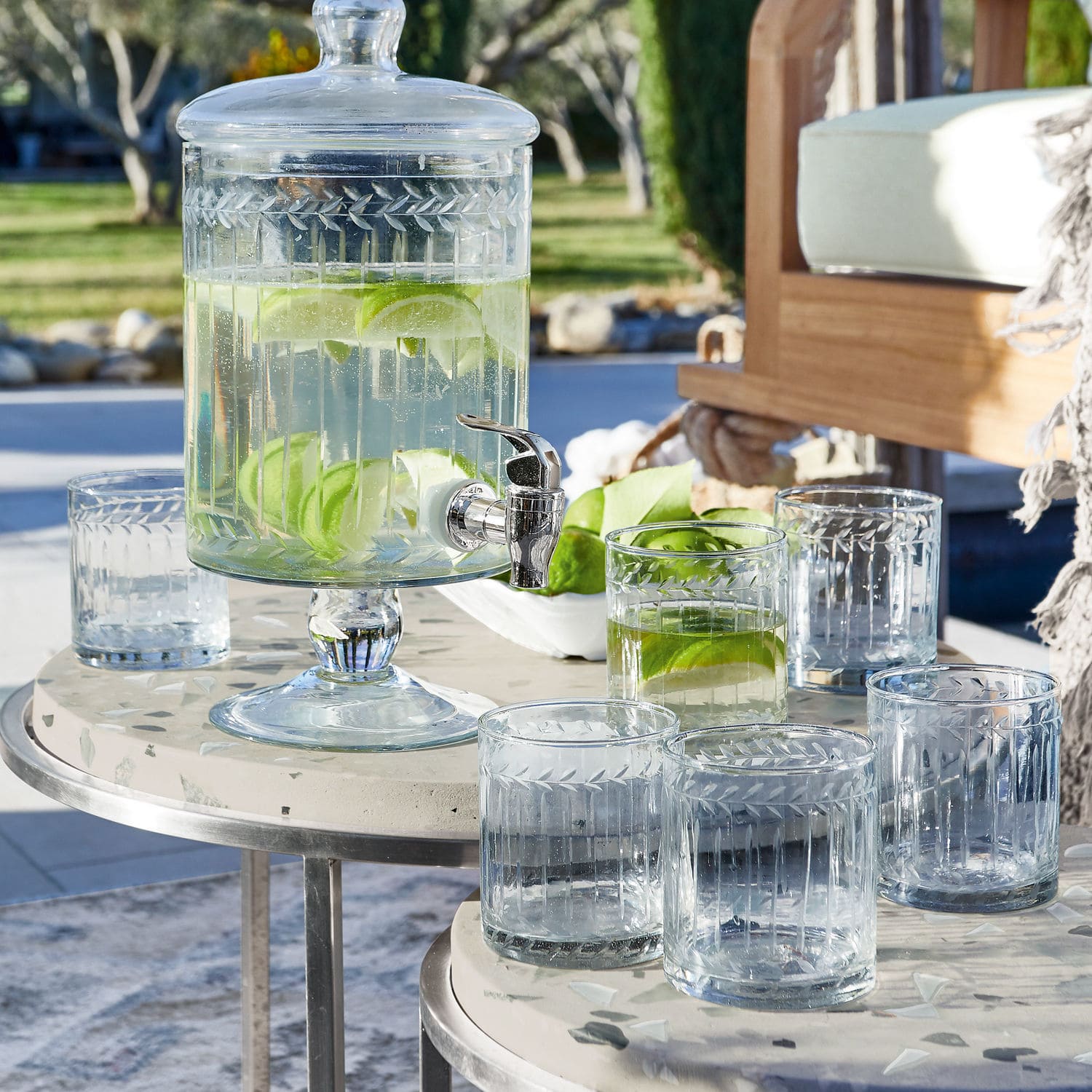 Glasgetränkespender mit Deckel und Zapfhahn, gefüllt mit Wasser und Limettenscheiben auf Terrasse