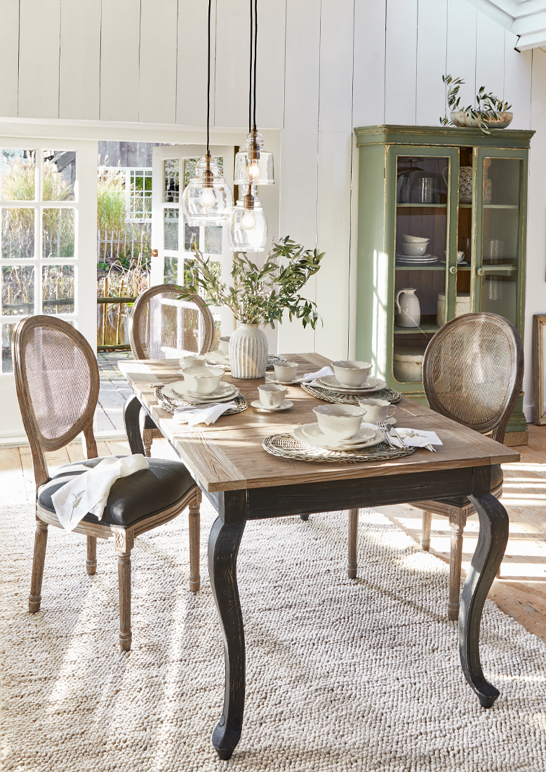 Esszimmer mit Holztisch und vintage Korbstühlen, natürliches Licht und stilvolle Dekorationen