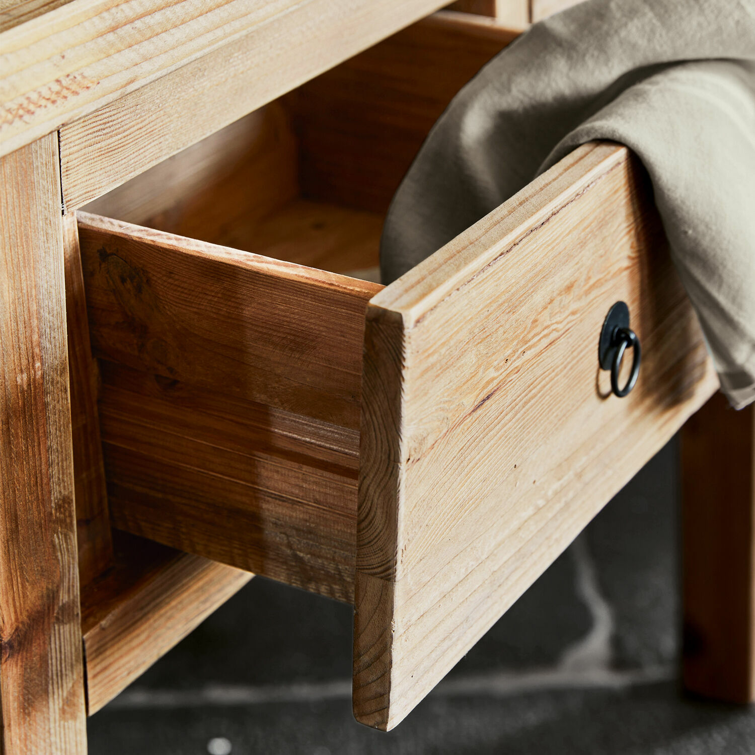 Offene Schublade aus hellem Holz mit schwarzem Metallgriff und grauem Stoff darauf