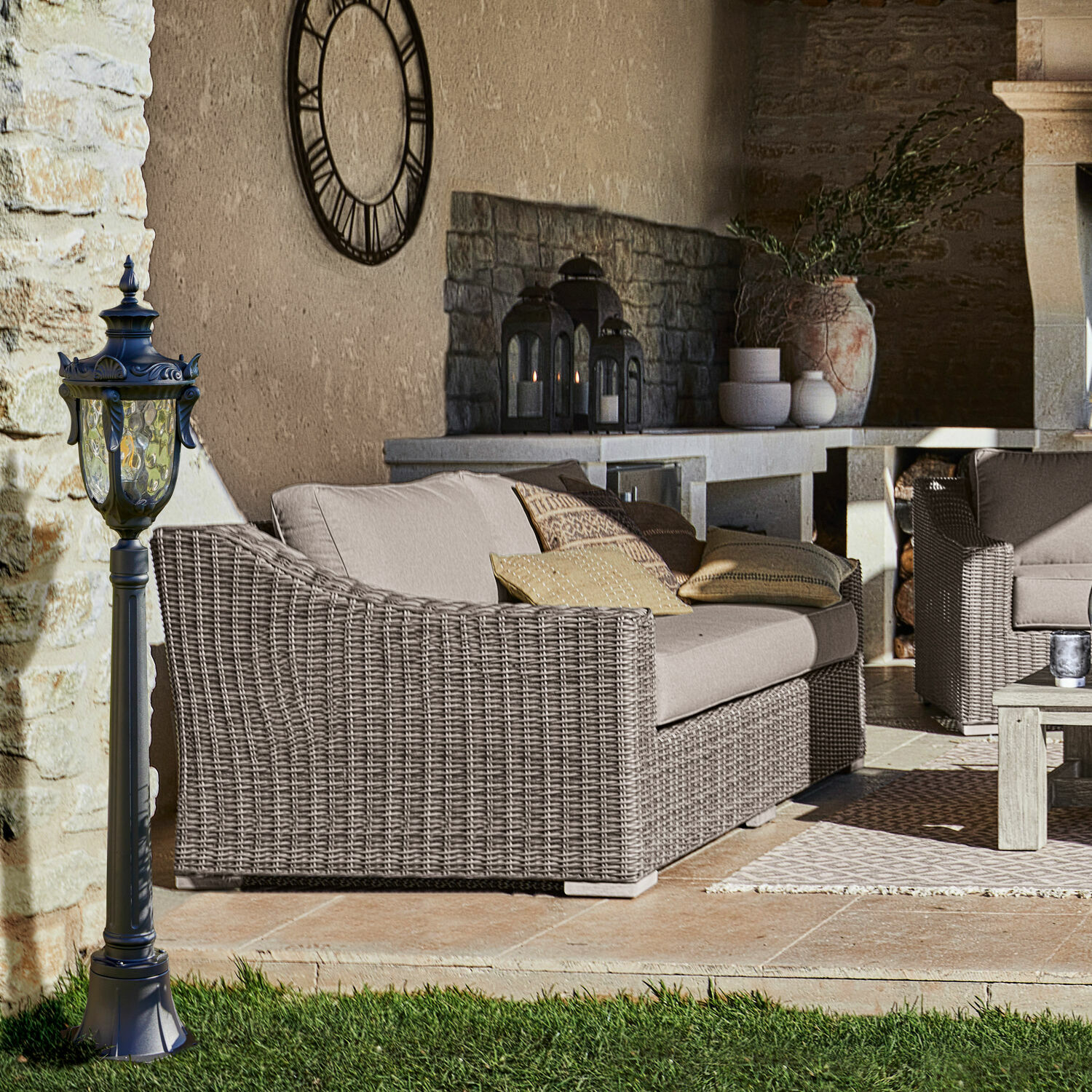 Garten mit grauem Rattansofa und schwarzer Außenlampe auf Rasen vor Steinmauer