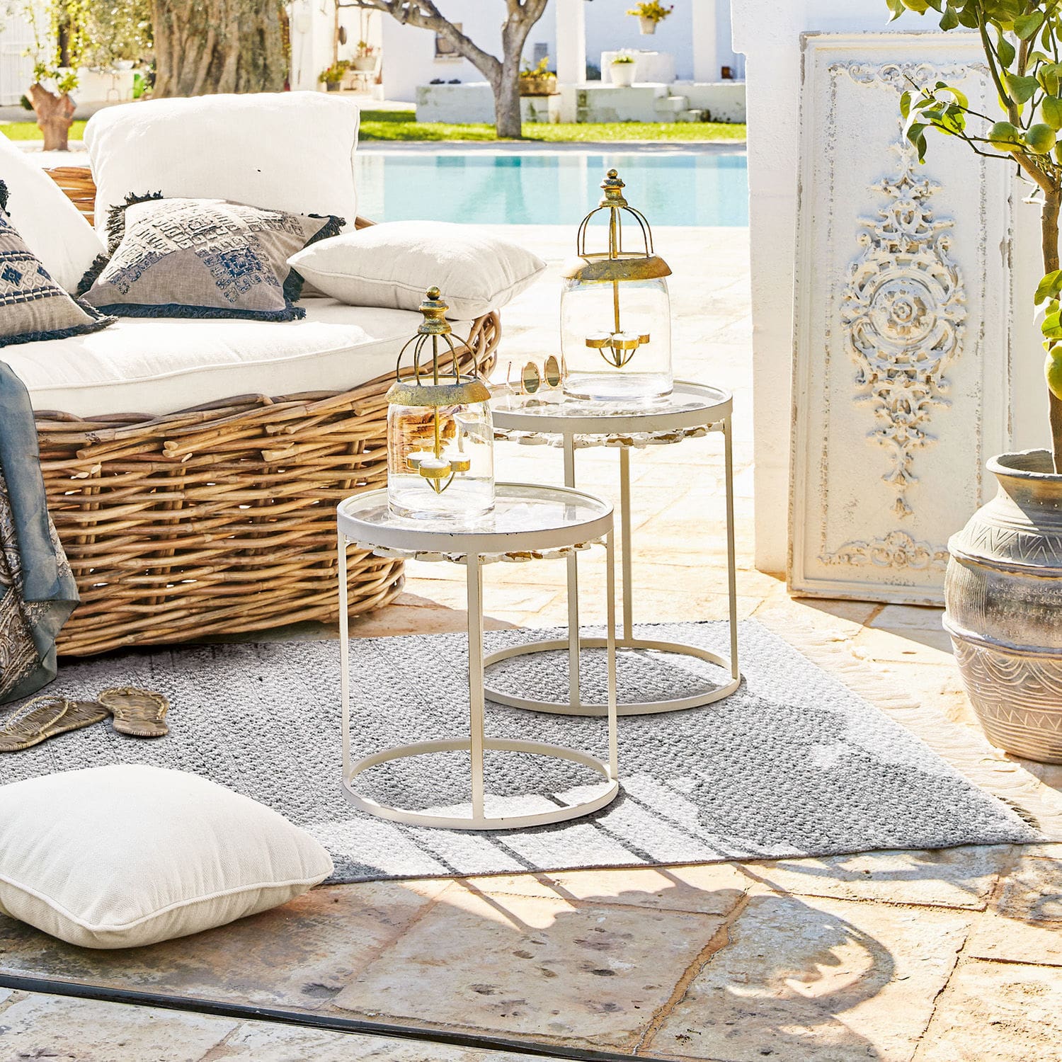Zwei weiße Metall-Beistelltische auf Terrasse mit Laternen und Rattansofa im Außenbereich