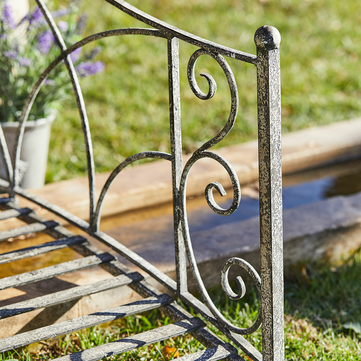 Gartenbank aus Metall mit grauer, antik wirkender Oberfläche und dekorativem Rückenlehreneinsatz