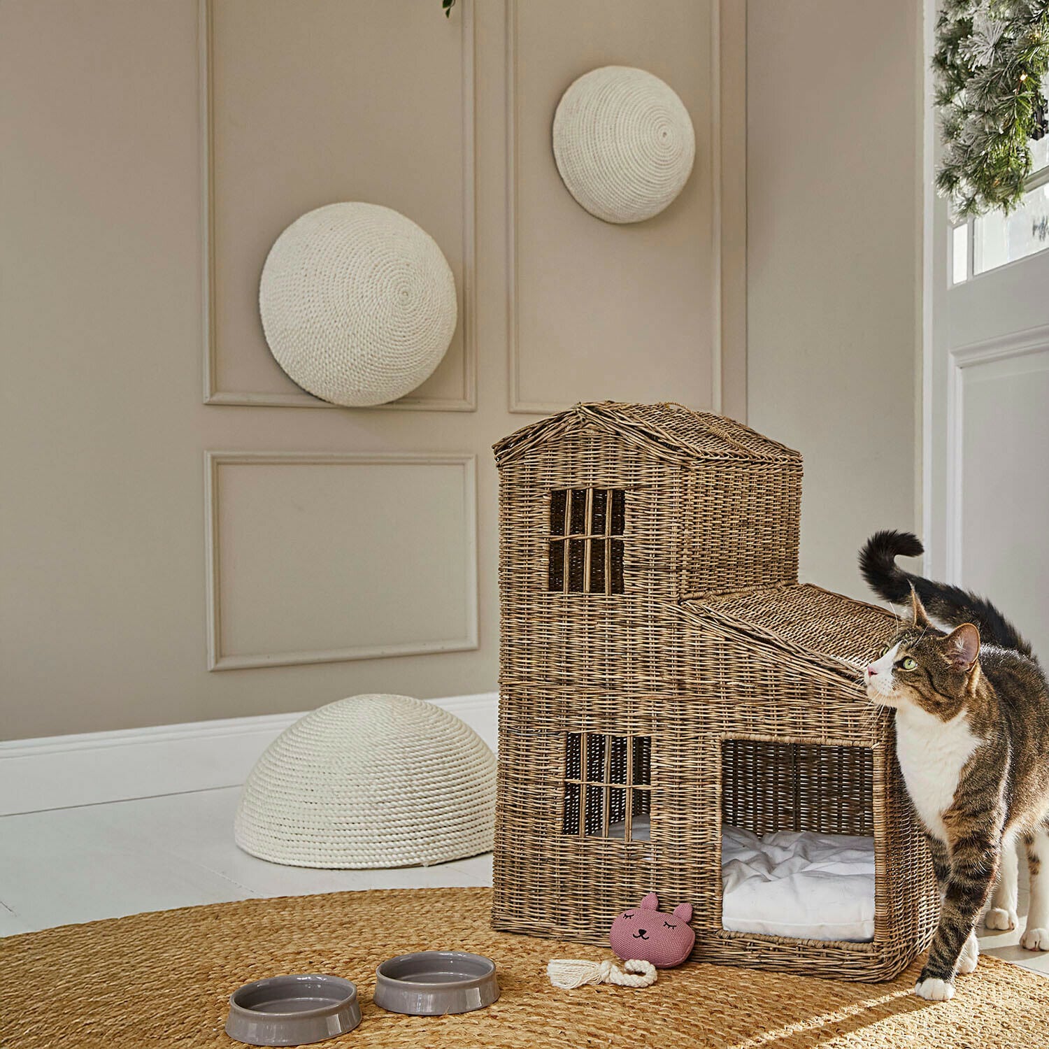 Katzenhaus aus natürlichem Weidengeflecht mit Kissen und Spielzeug, Futternäpfe auf Teppich