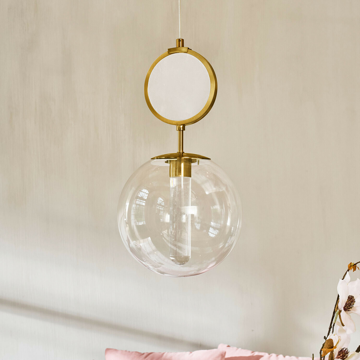 LED-Hängelampe Corvane Goldene Pendelleuchte mit klarem Glaskugel und rundem dekorativem Element vor hellem Wandhintergrund
