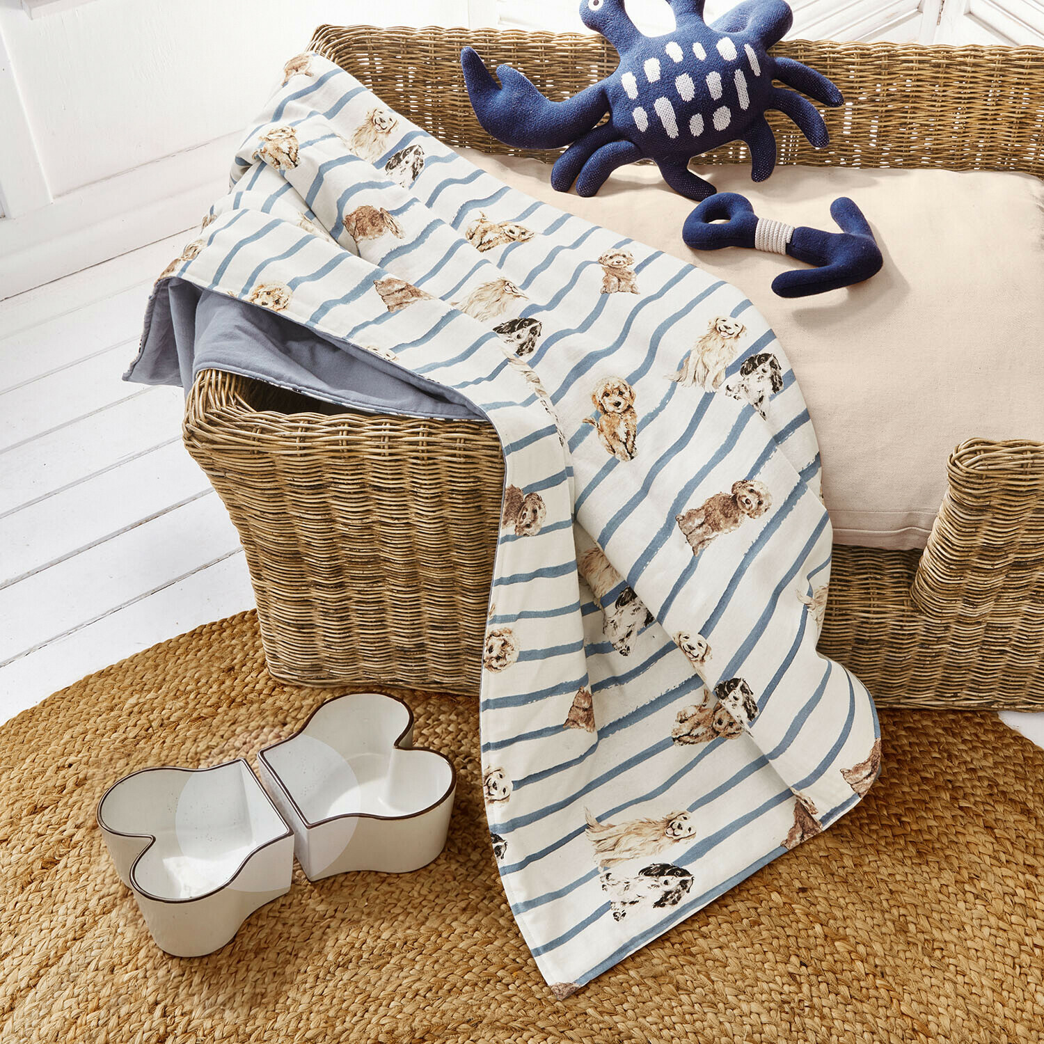 Hundeplaid Schnuffelex Hundedecke mit blauen Streifen und Hunde-Motiv auf Korb mit Spielzeug und Futternapf aus Keramik