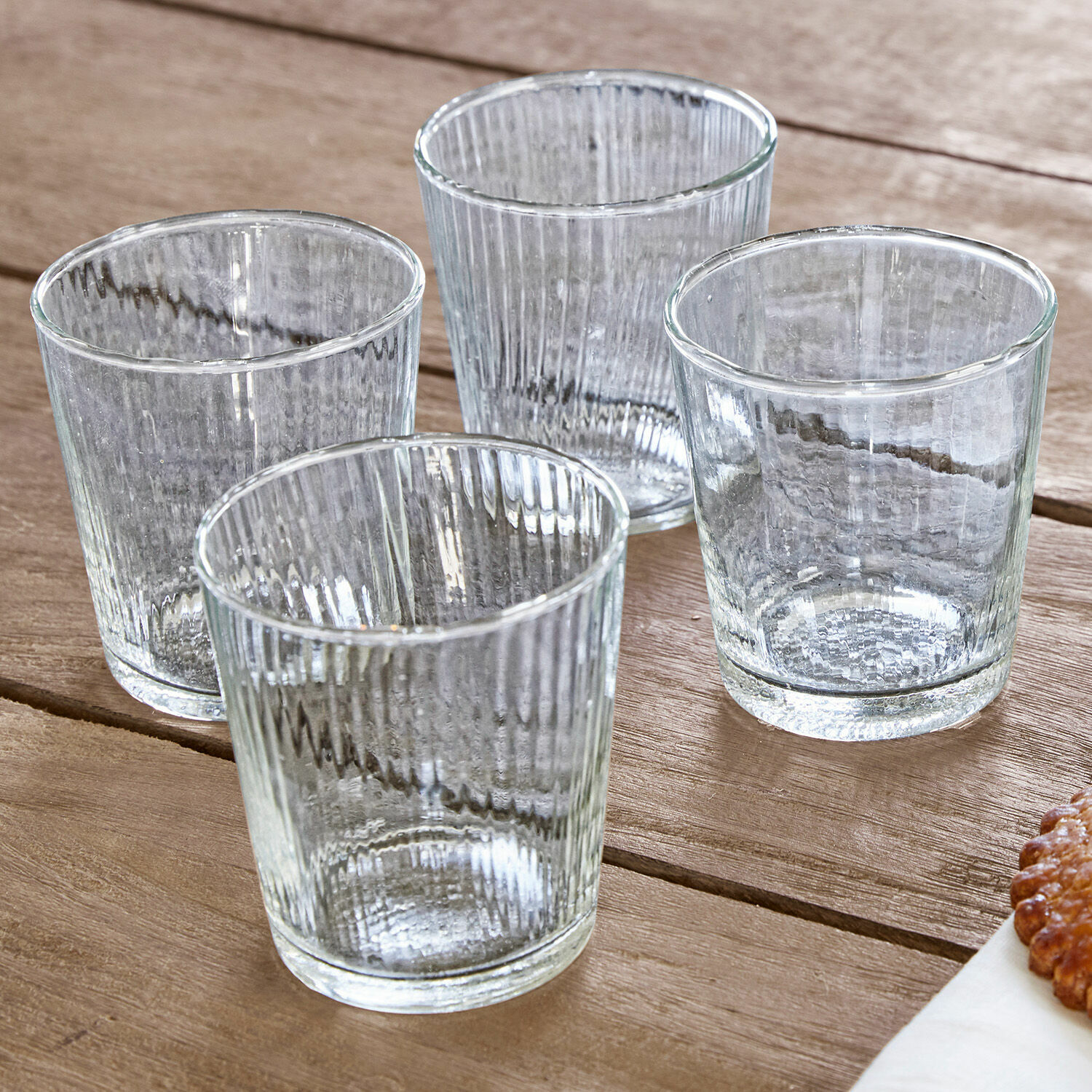 Set aus vier transparenten Trinkgläsern aus geriffeltem Glas auf Holztisch, Trinkgläser