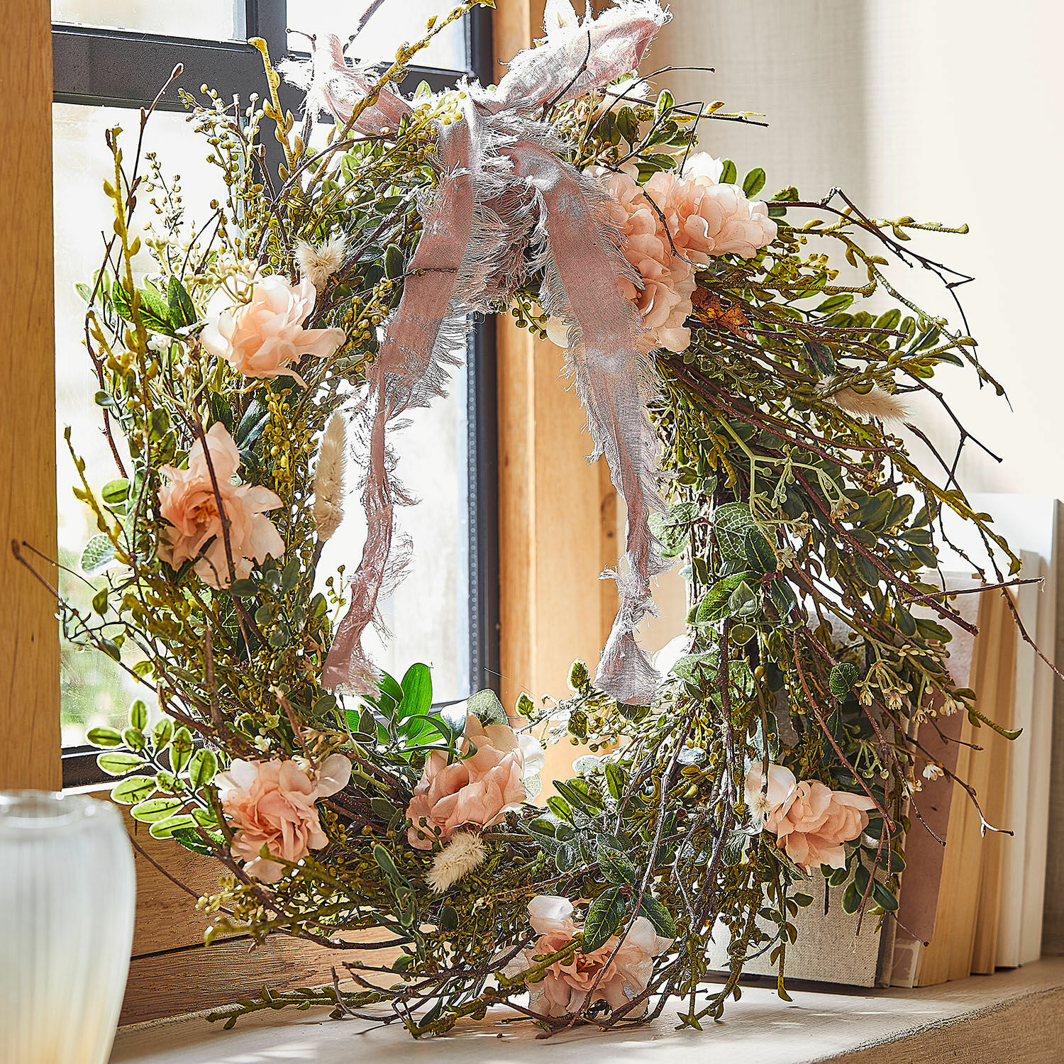Kranz Chérisse Dekorativer Kranz aus Zweigen, rosa Blüten und grünen Blättern mit rosa Band am Fenster