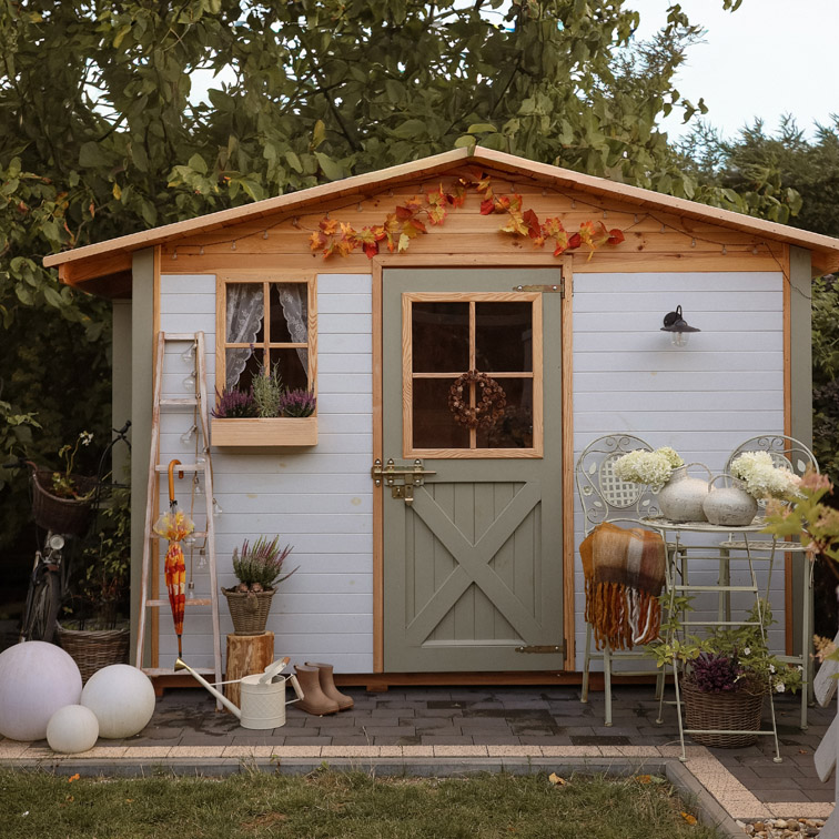 Helles Holz-Gartenhaus mit grüner Tür und herbstlicher Dekoration im Garten