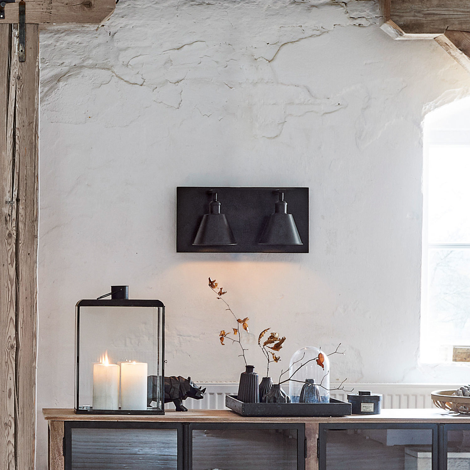 Schwarze Metall-Wandleuchte mit zwei konischen Lampenschirmen an rustikaler Wand mit Dekoration