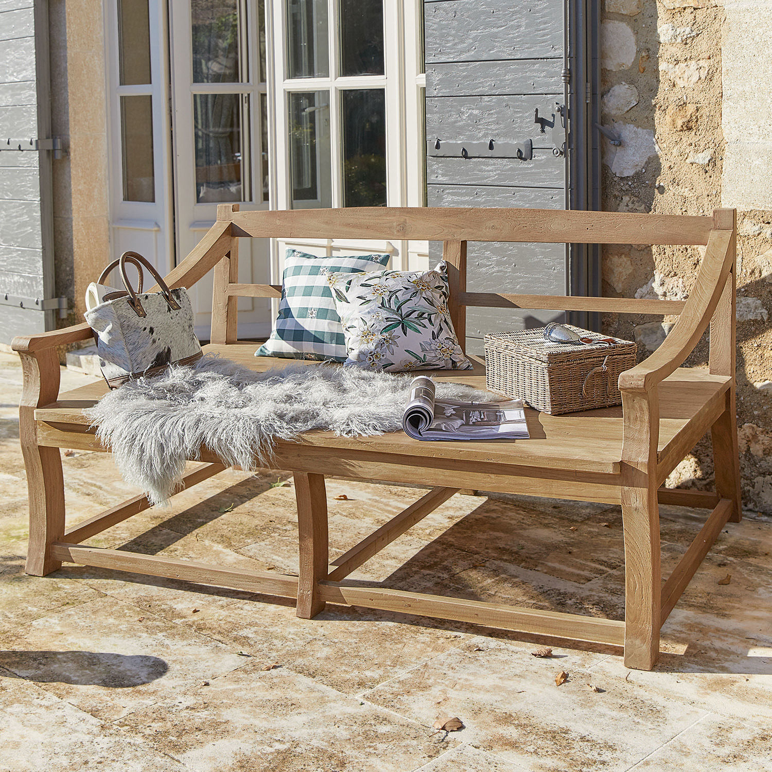 Dreisitzige Teakholzbank in Naturfarbe auf Terrasse mit Kissen und grauem Fell