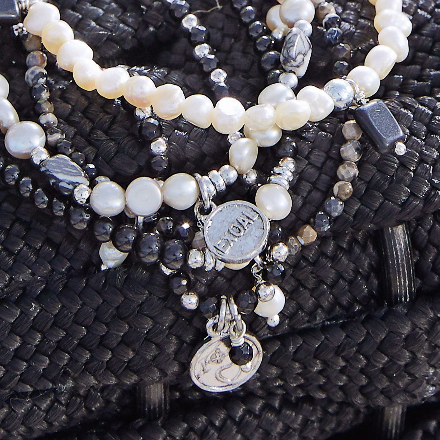 Perlen- und schwarze Steinarmbänder mit Metallanhängern auf schwarzem Hintergrund, Damenschmuck