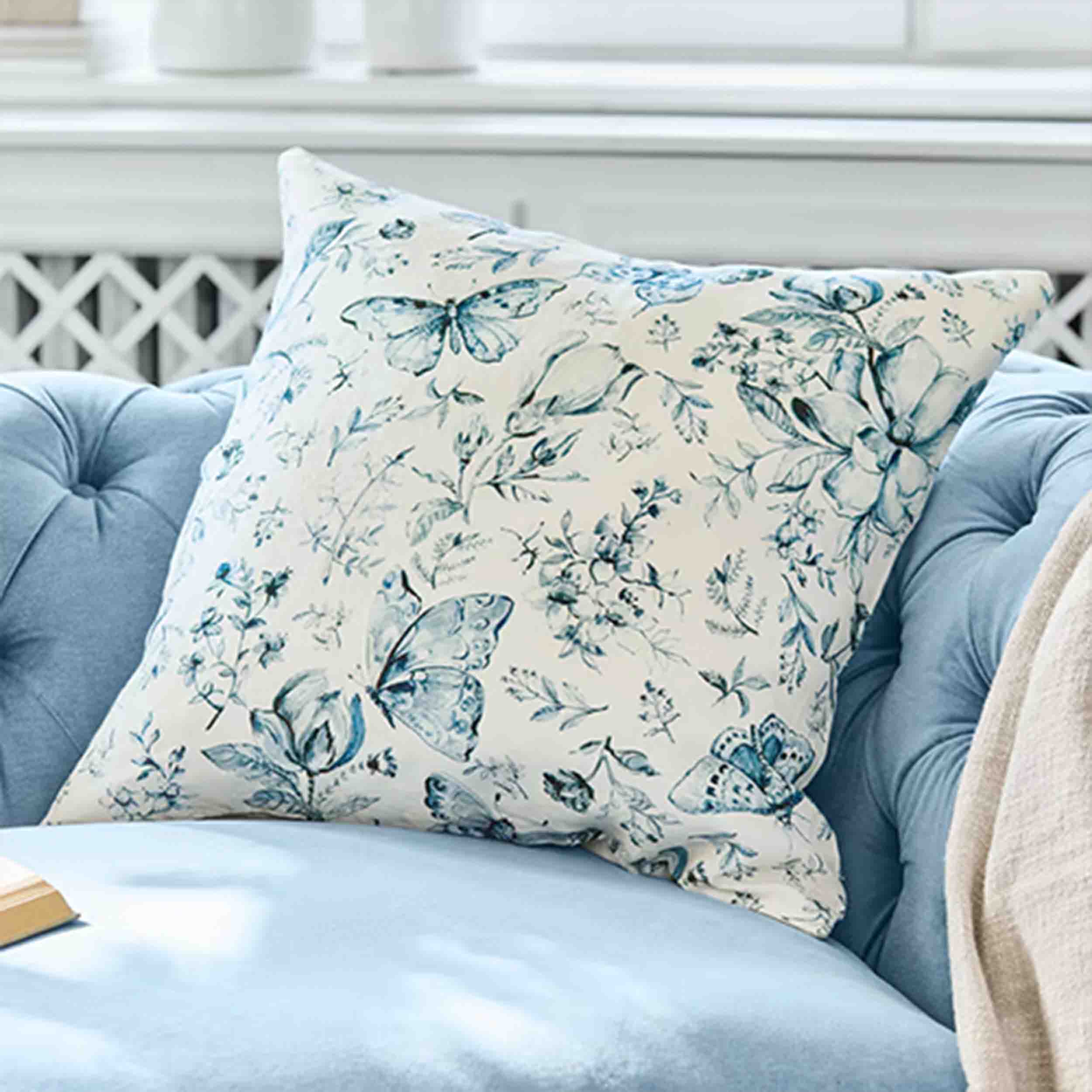 Dekoratives Baumwollkissen in Creme mit blauem Schmetterlings- und Pflanzenmuster, Wohntextilien