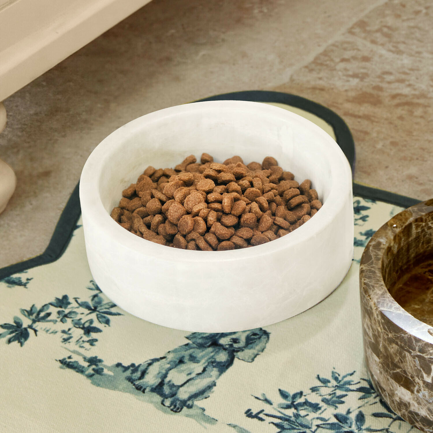 Weiße Marmorschale mit braunem Tierfutter auf dekorativer Unterlage mit Hundemotiv