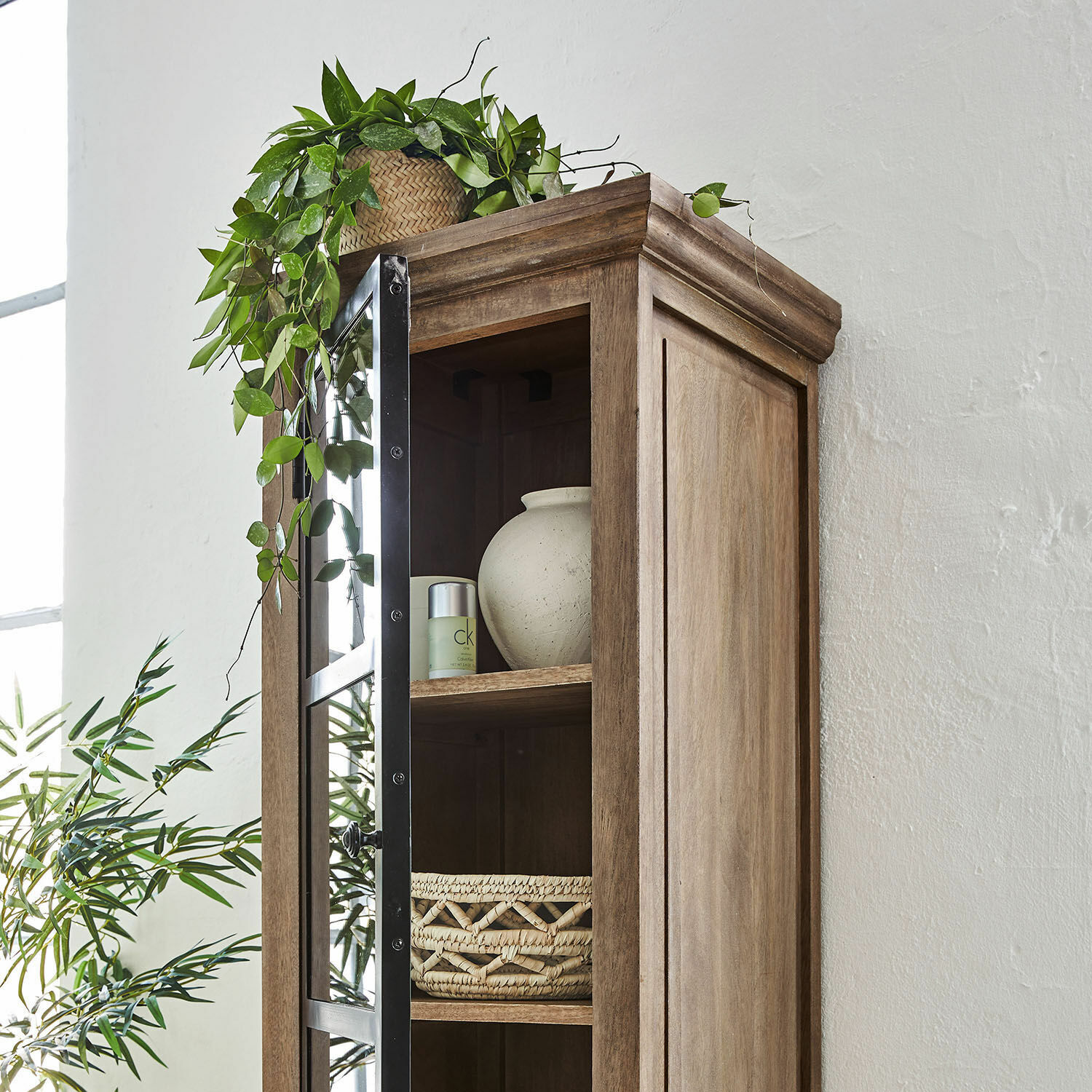 Holzvitrine mit Glastür und Metallrahmen, dekoriert mit grüner Pflanze und geflochtenem Korb