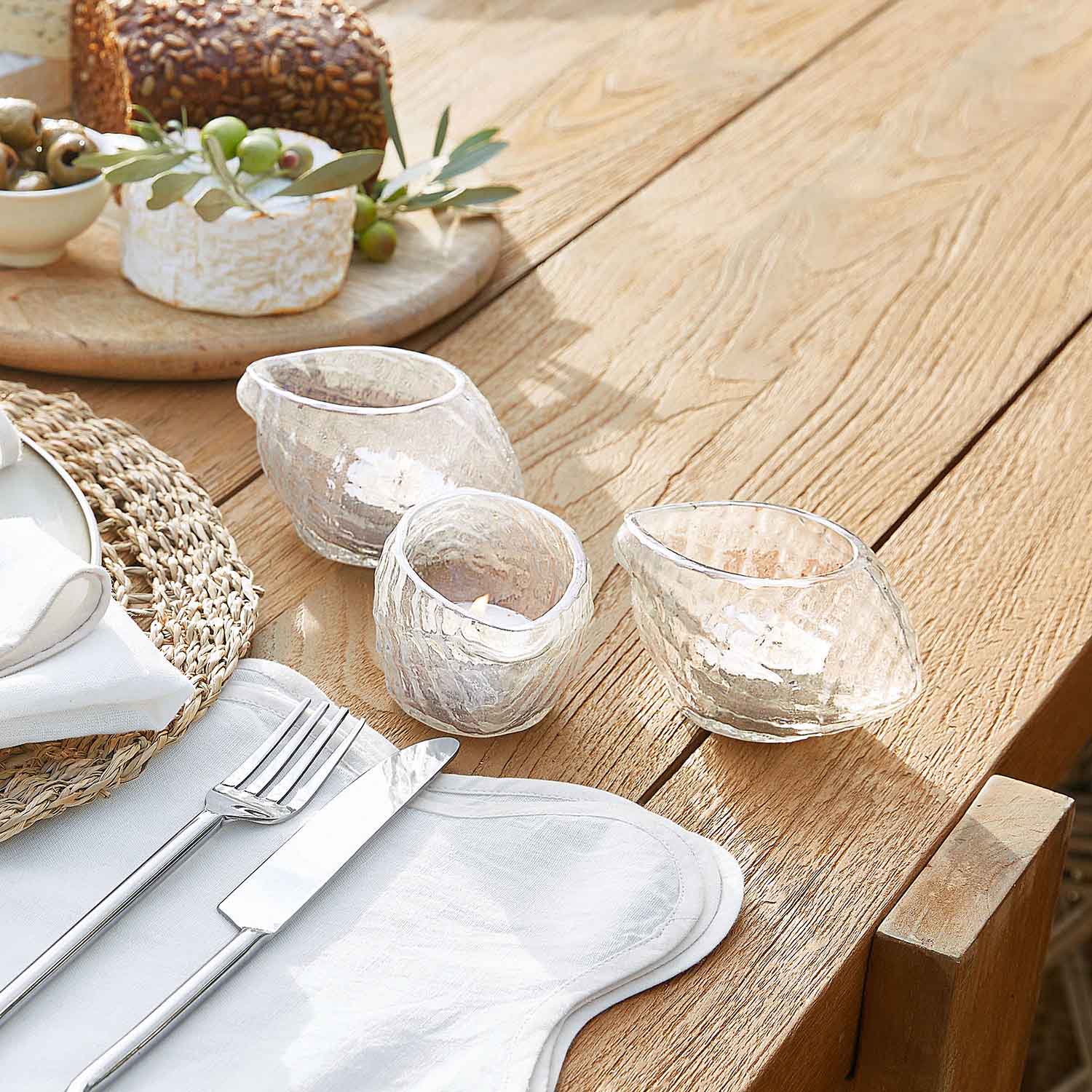 Set aus drei transparenten Glas-Teelichthaltern mit unregelmäßiger Form auf hellem Holztisch