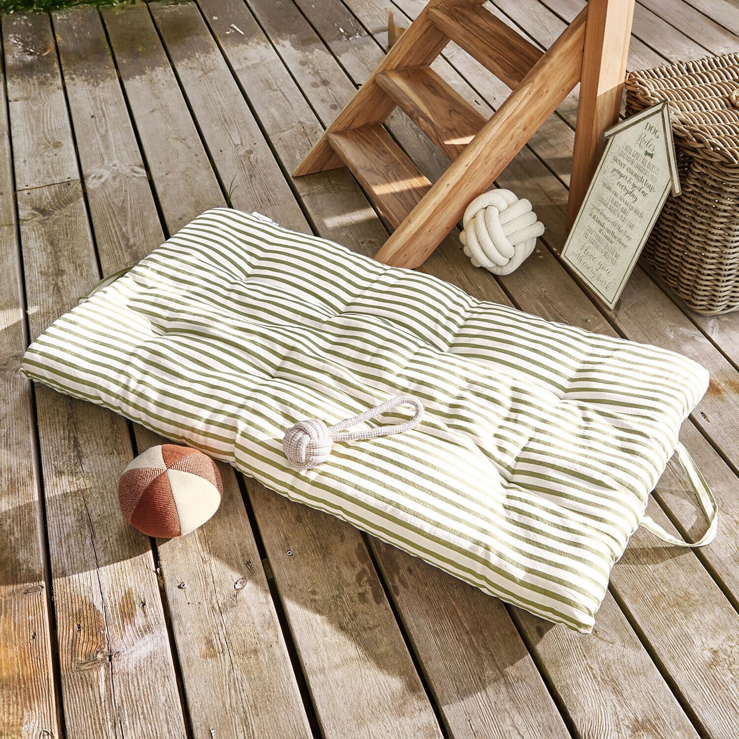 Gepolstertes grün gestreiftes Bodenkissen auf Holzterrasse mit Hundespielzeug