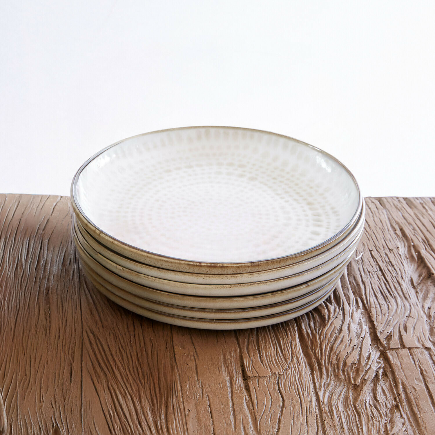 Set aus sechs cremefarbenen Keramiktellern mit feinem Muster auf einem Holztisch