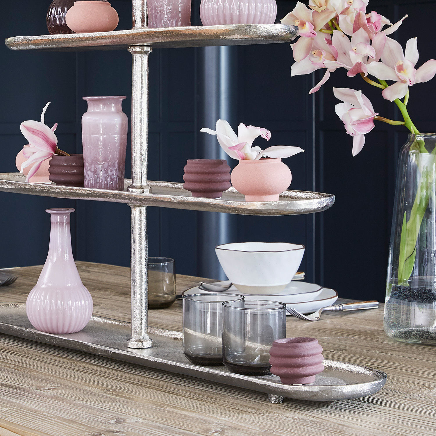 Dreistöckiges silbernes Tablett mit rosa und violetten Vasen und Gläsern auf Holztisch