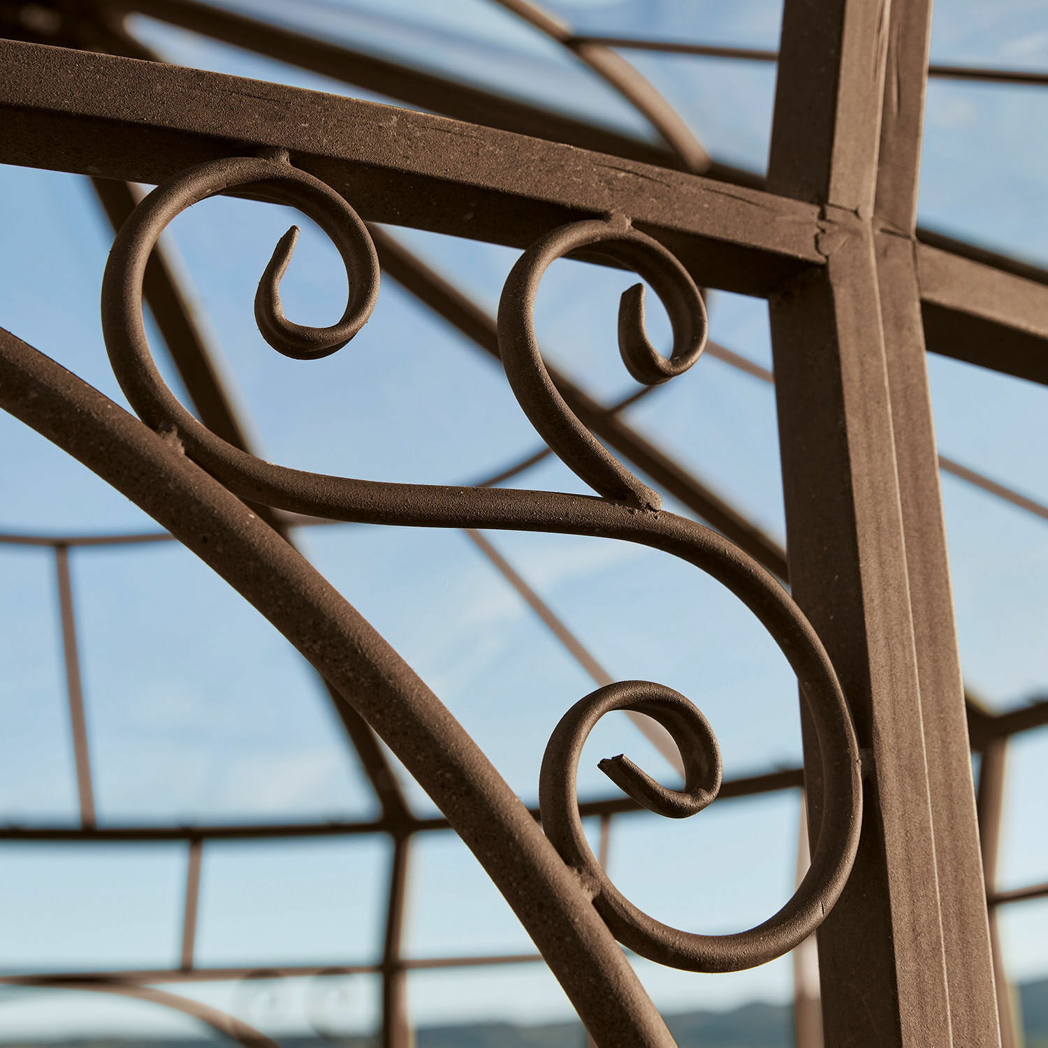 Braune Metallkonstruktion mit dekorativen Schnörkeln vor blauem Himmel, Gartenelement