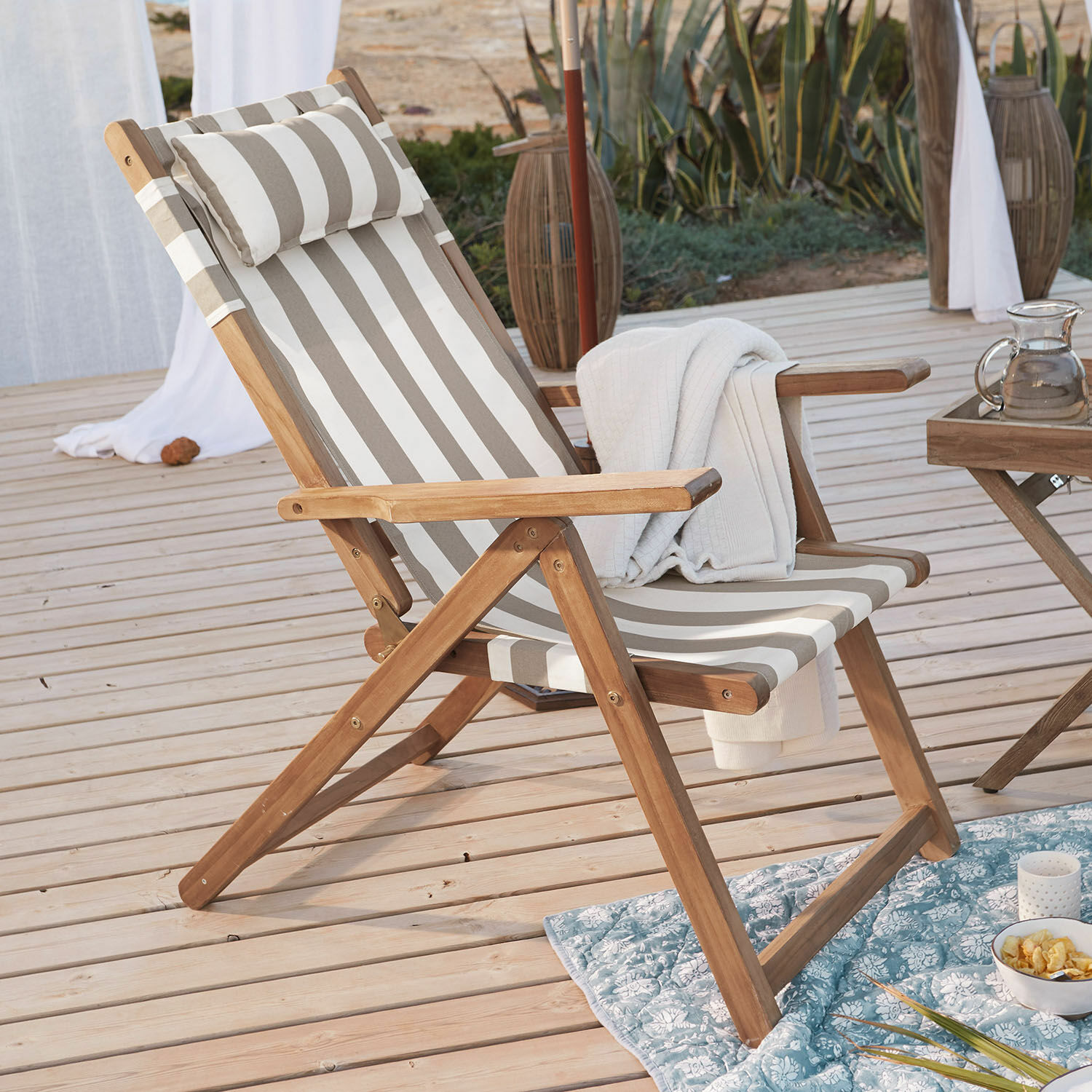 Gartenliege aus Holz mit beige-weiß gestreiftem Stoff auf Holzterrasse mit Decke und Snacks