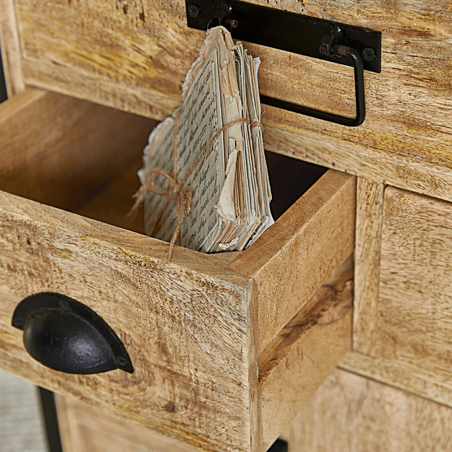 Offene Schublade aus hellem Mangoholz mit schwarzem Metallgriff und gebündelten alten Briefen.
