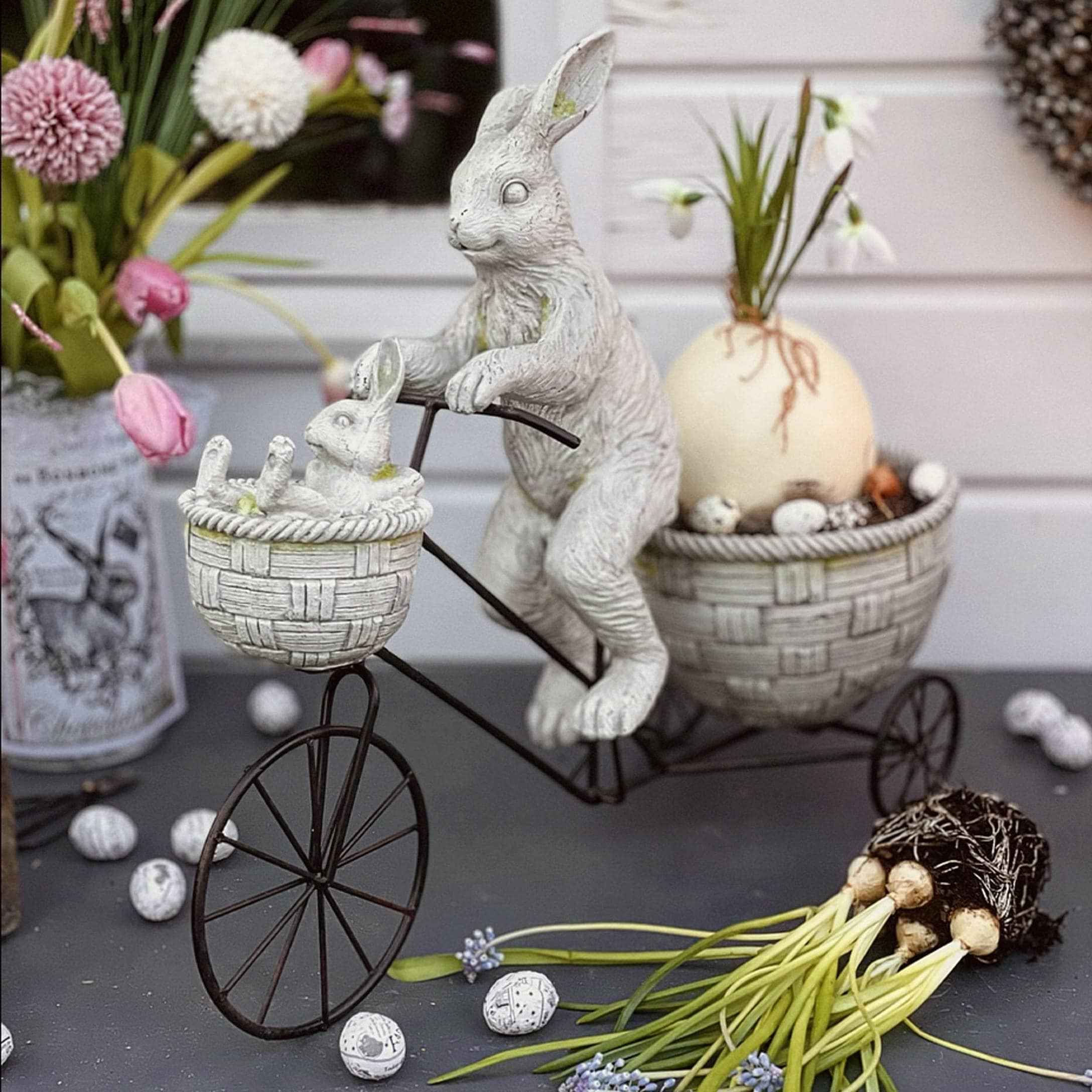 Osterdekoration mit weißen Hasen aus Kunststoff auf Metallfahrrad mit Körben und Blumen