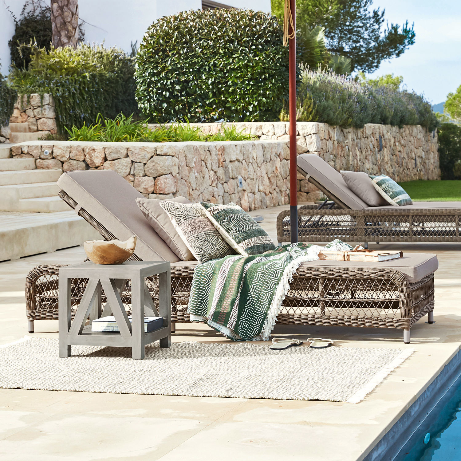 Beiger Rattan-Liegestuhl mit Kissen und grünem Deckenmuster am Pool im Garten