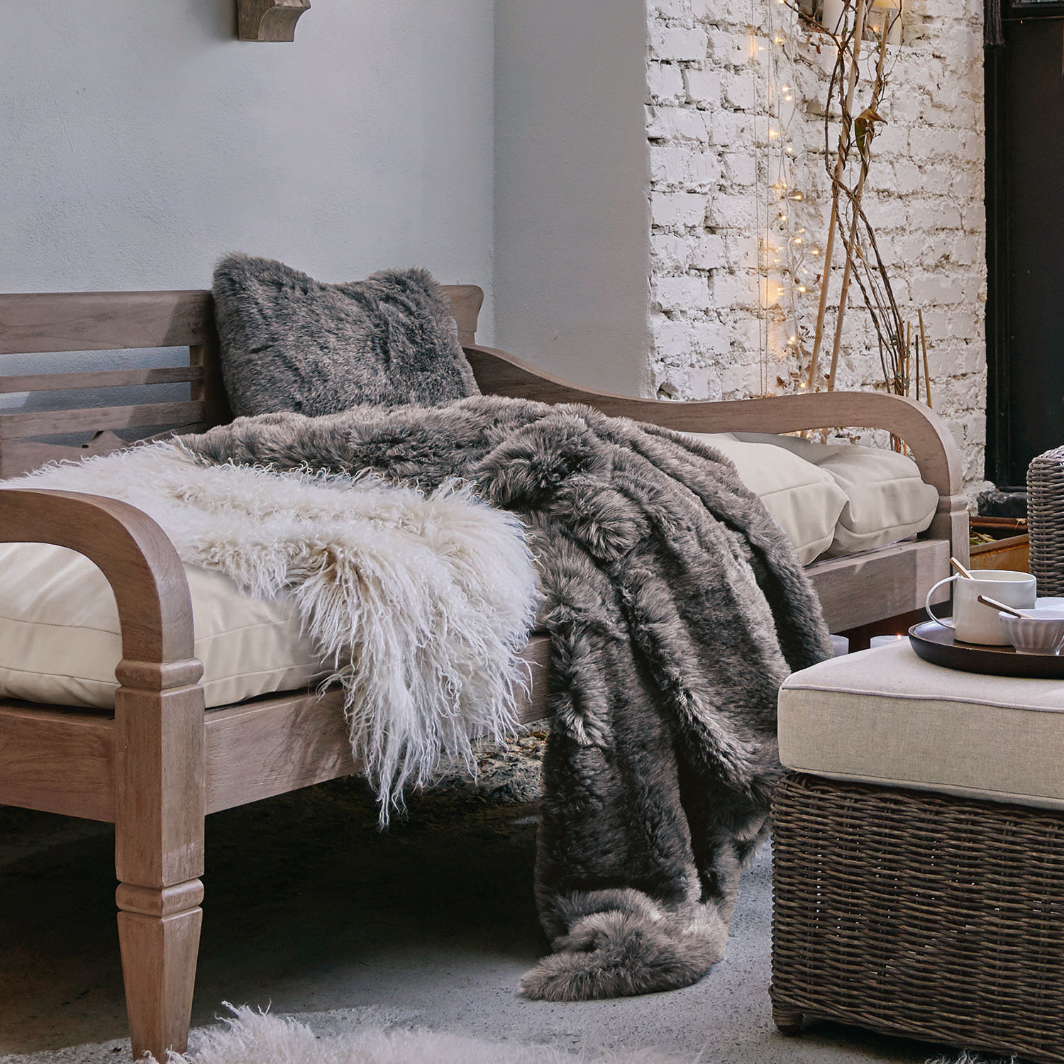Holzsofa mit cremefarbenem Kissen und weichen grauen und weißen Fell-Decken für gemütliches Ambiente
