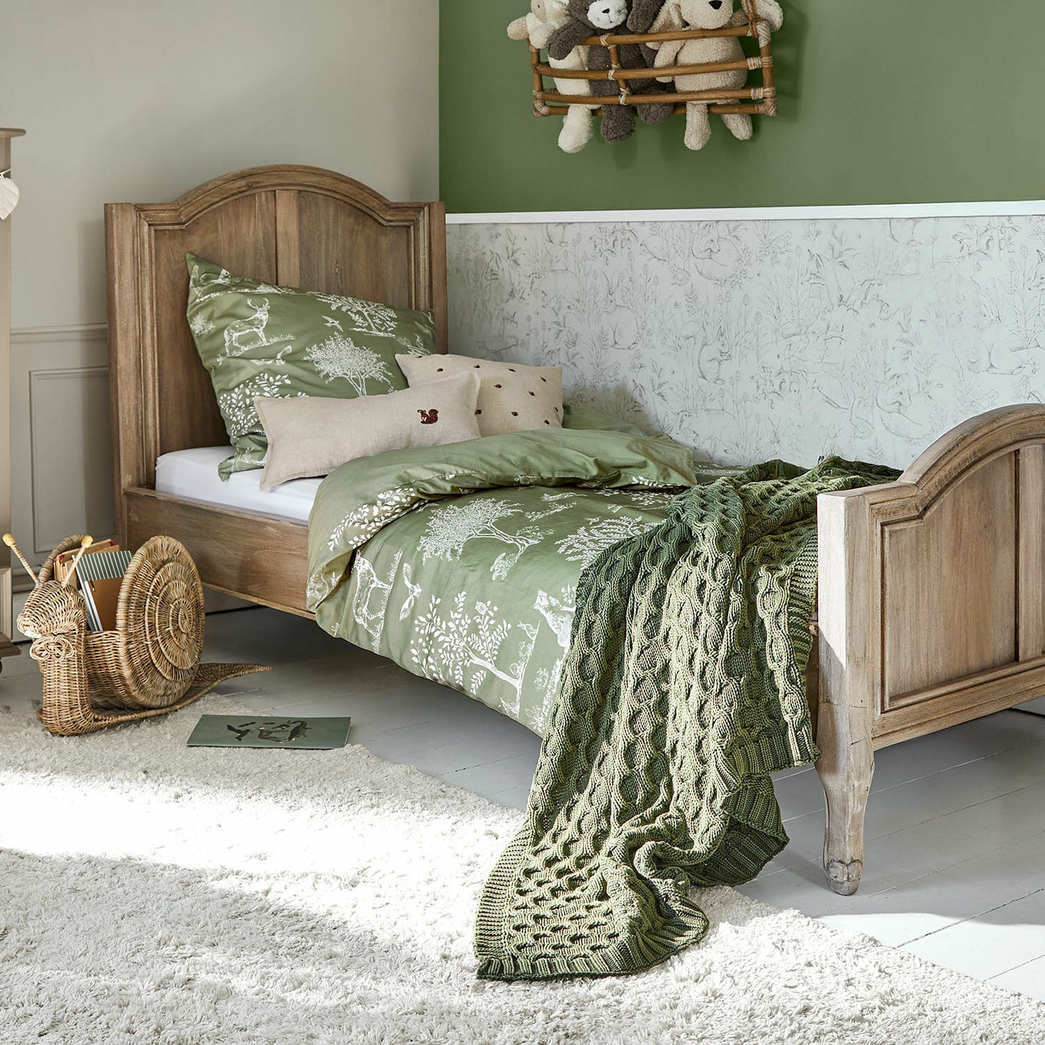 Kinderbett aus Holz mit grüner Tiermuster-Bettwäsche und gestrickter Decke im Kinderzimmer