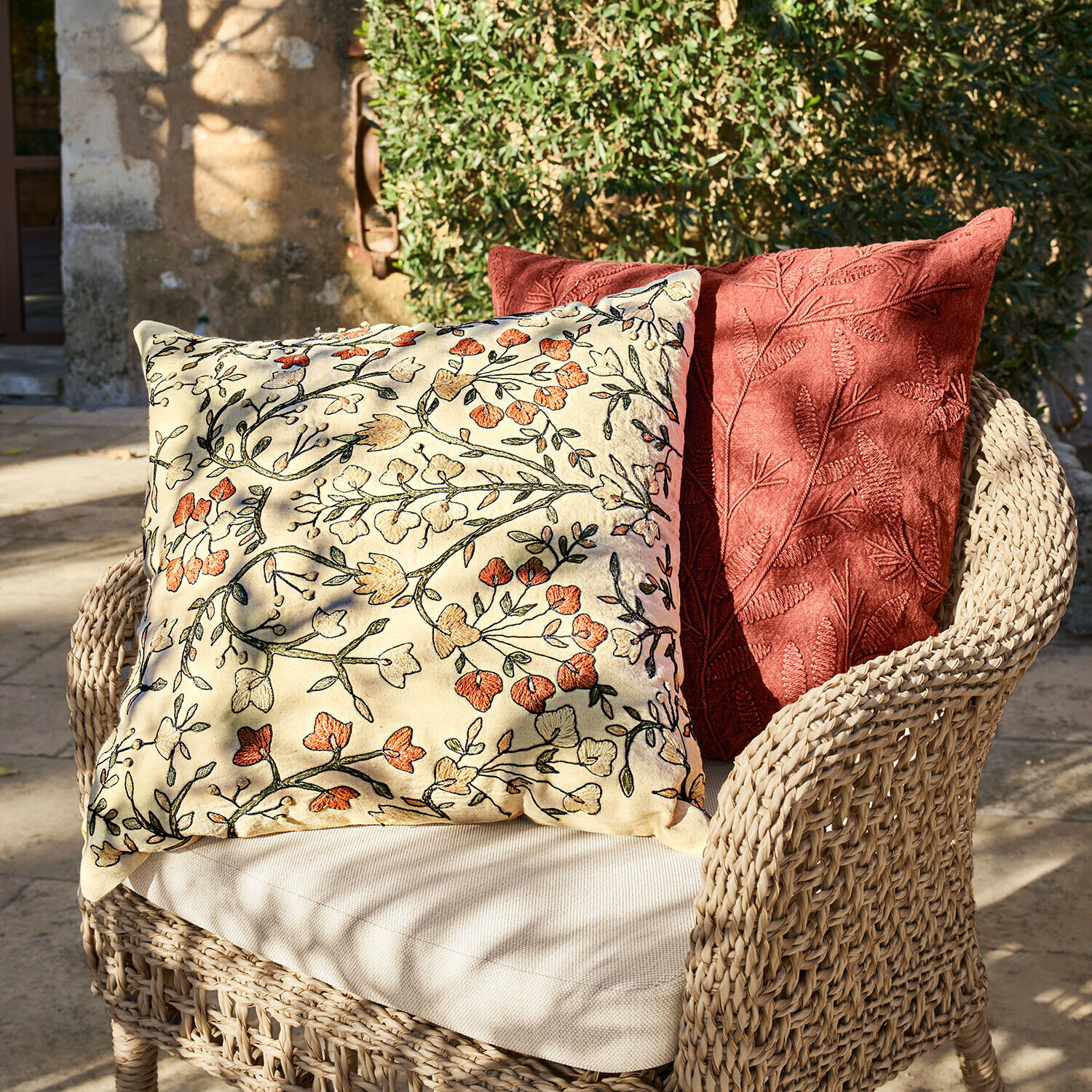 Zwei dekorative Kissen mit Blumen- und Blattstickerei auf einem Korbsessel im Außenbereich
