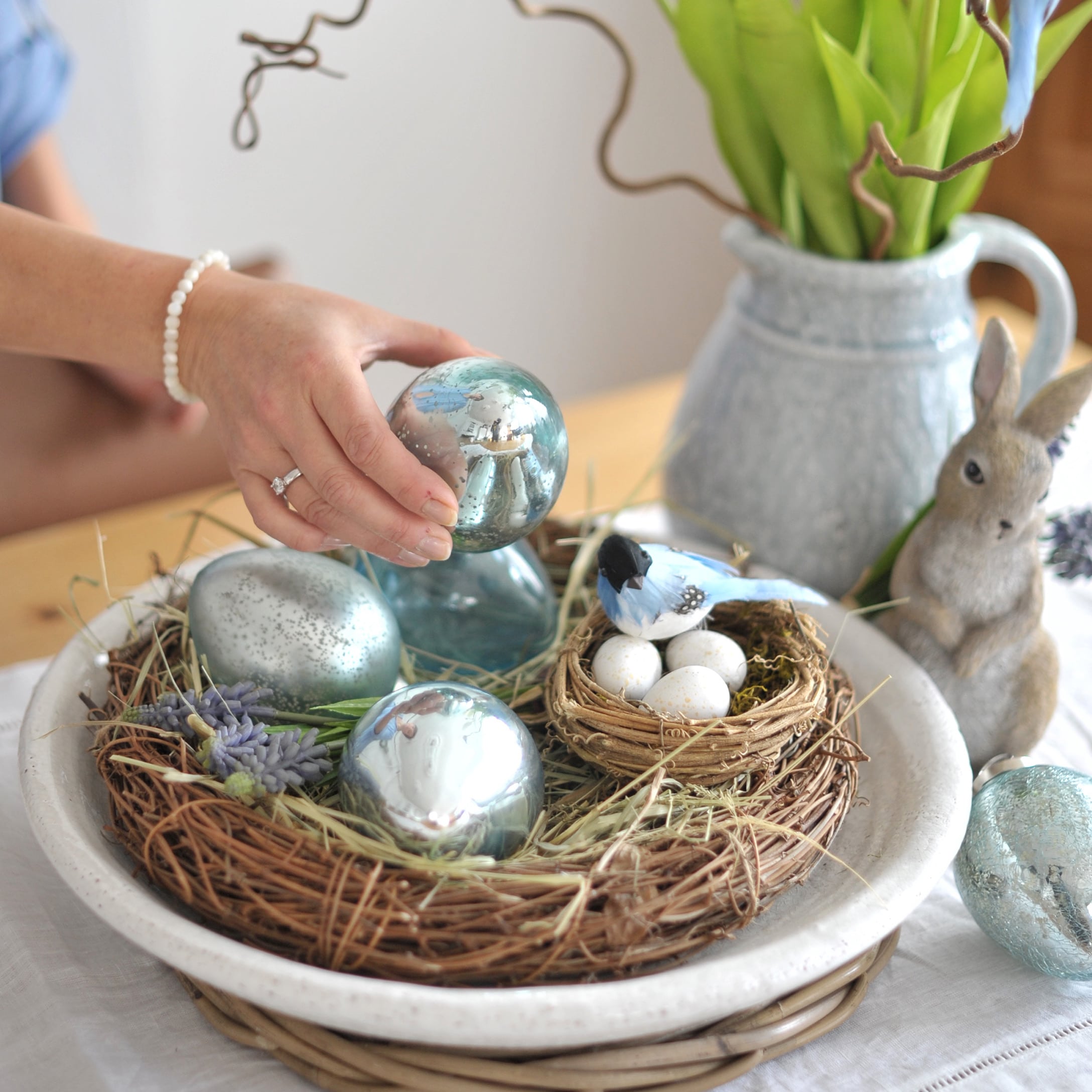 Osterdekoration mit blauen Glaseiern und Nest mit weißen Eiern auf einem Holztisch