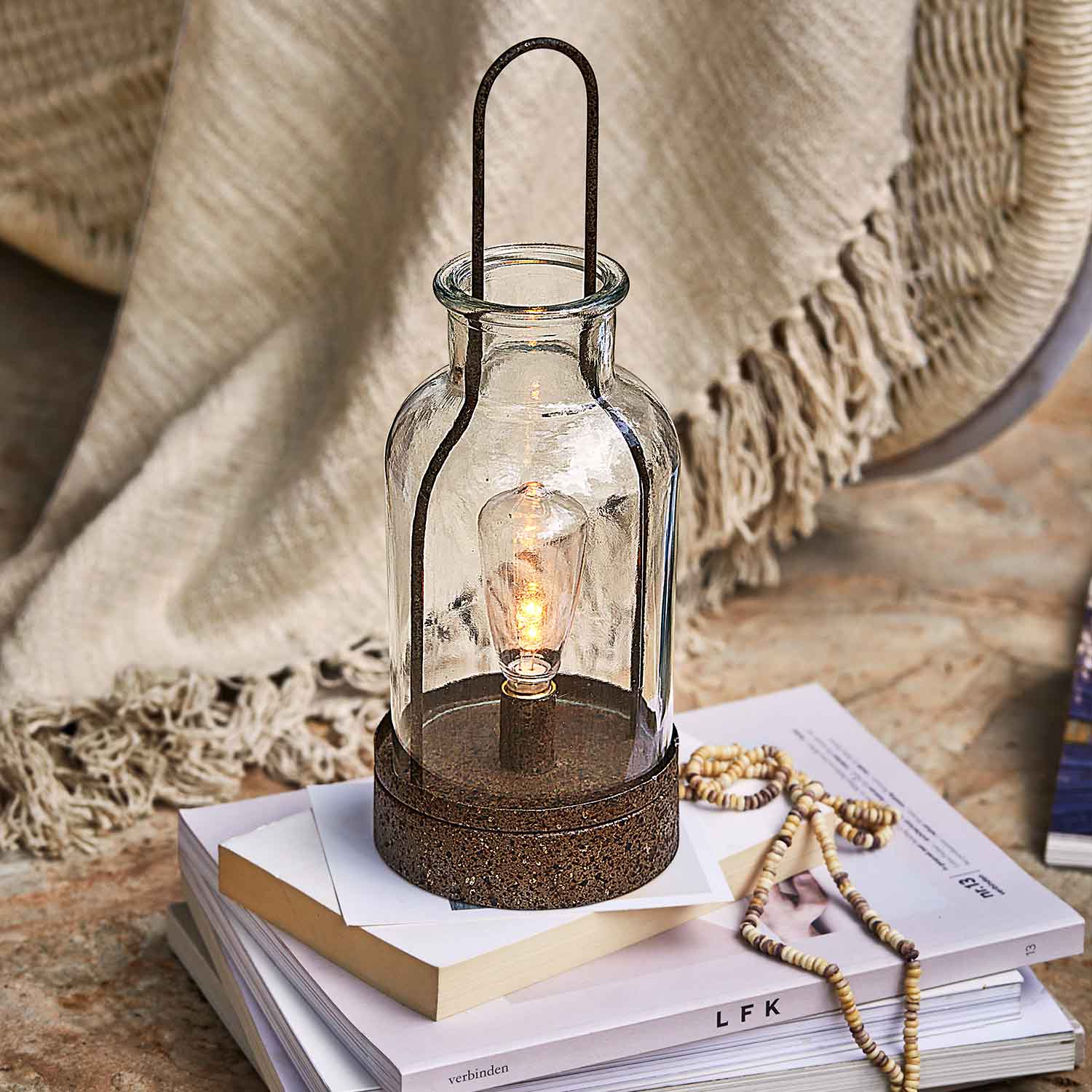 Glaslaterne mit rostfarbener Metallbasis auf Bücherstapel, Wohnaccessoire und Lichtquelle