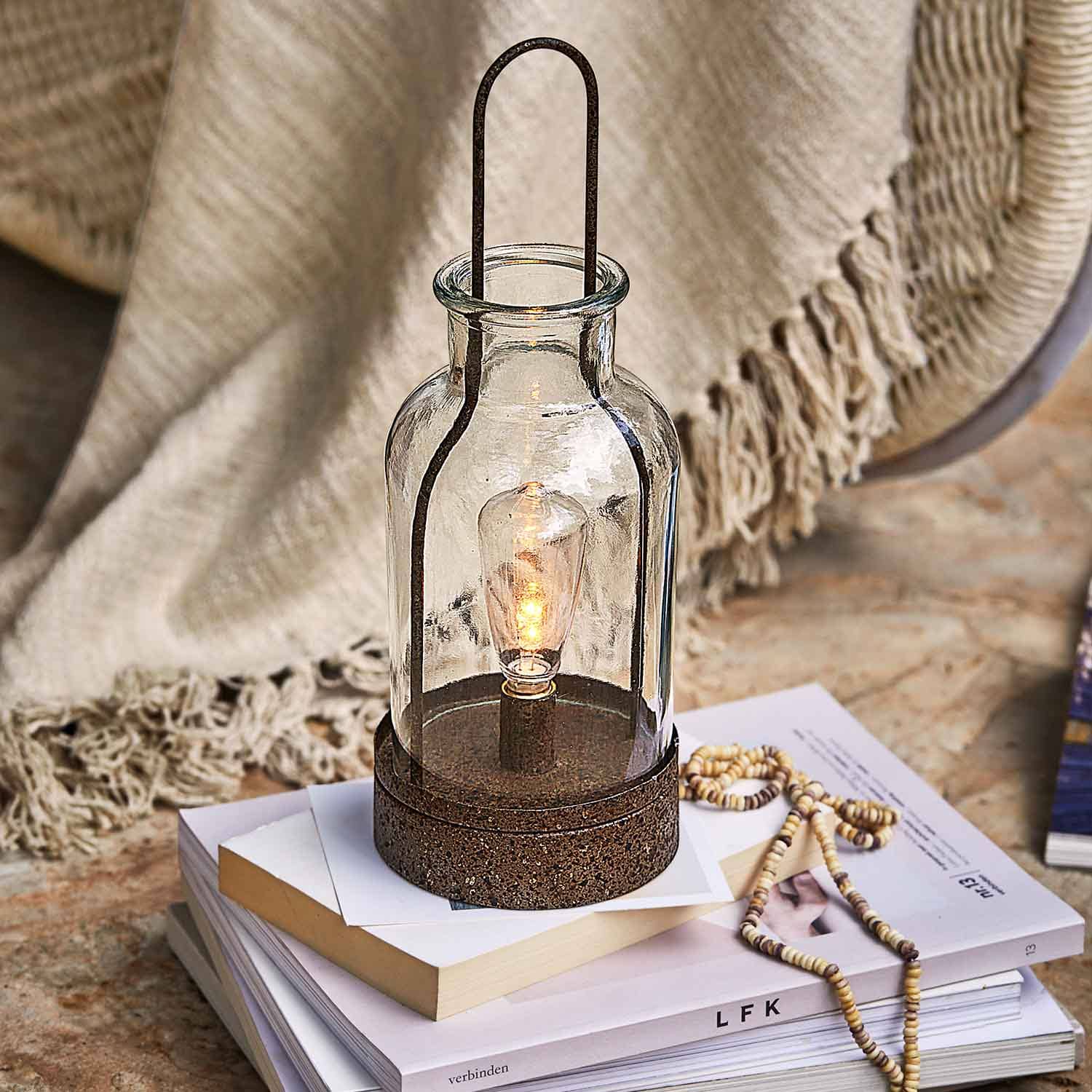 Glaslaterne mit rostfarbener Metallbasis auf Bücherstapel, Wohnaccessoire und Lichtquelle