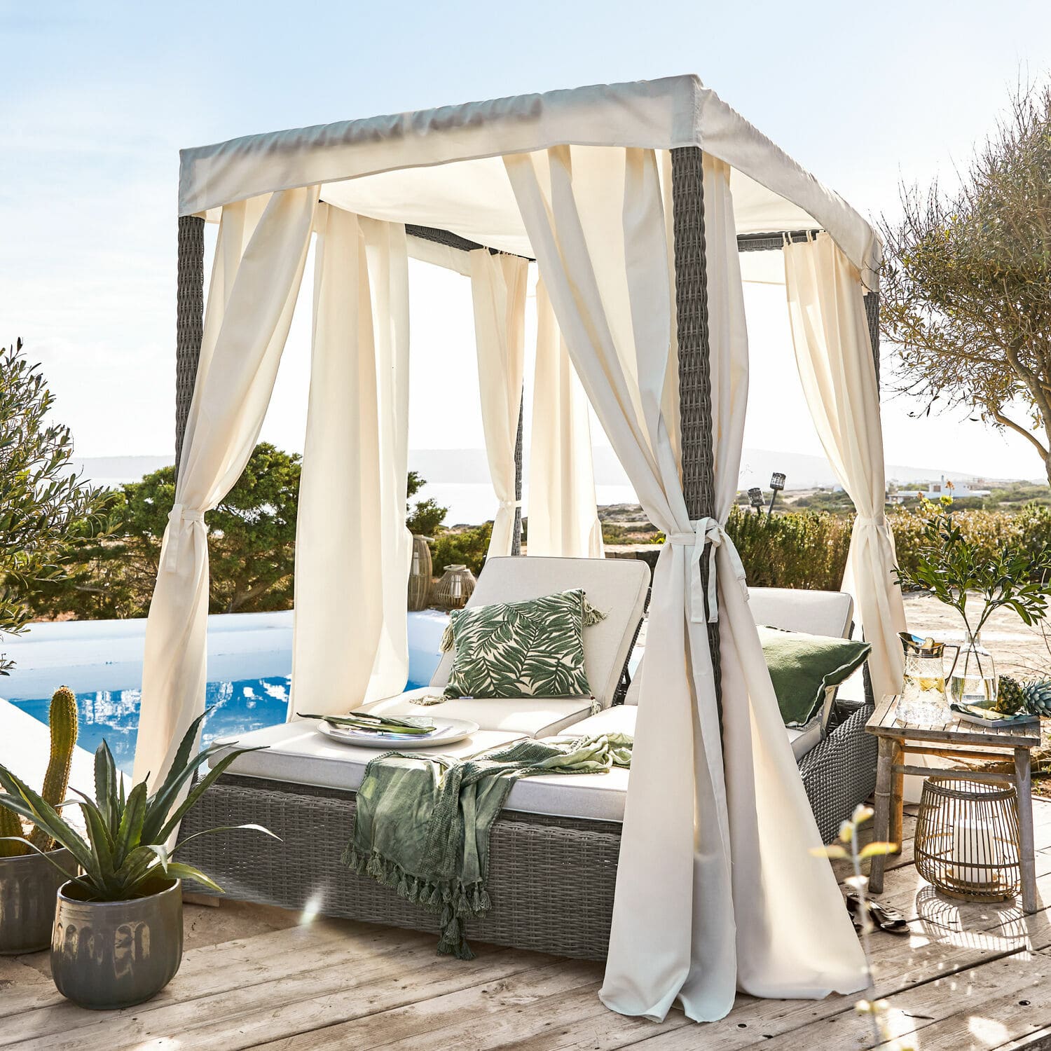 Graues Rattan-Sonnenbett mit cremefarbenem Baldachin und Vorhängen auf Holzterrasse am Pool