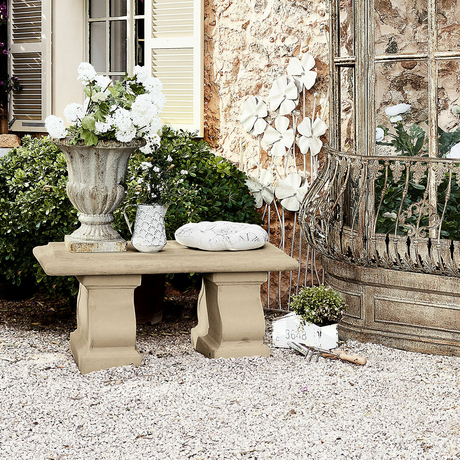 Beige Gartenbank aus Stein auf Kies mit dekorativen Pflanzgefäßen und grüner Bepflanzung