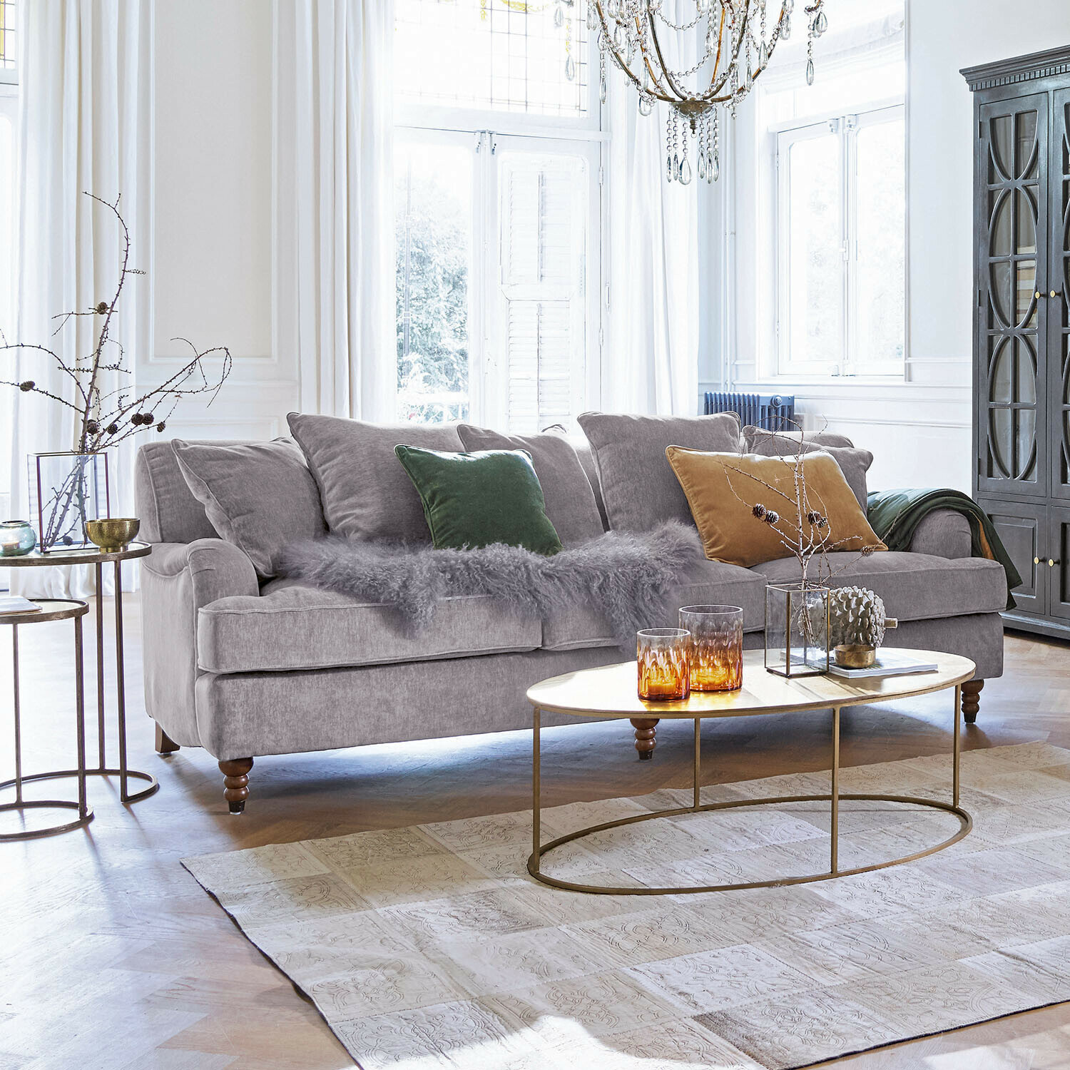 Graues Sofa aus weichem Stoff mit bunten Kissen und ovalem Couchtisch im hellen Wohnzimmer