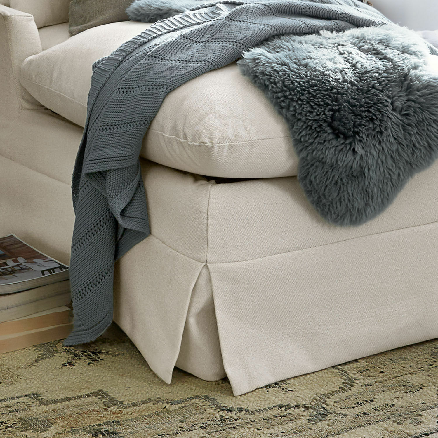 Beige Stoffecke mit grauer Strickdecke und weichem Fellplaid auf gemustertem Teppich