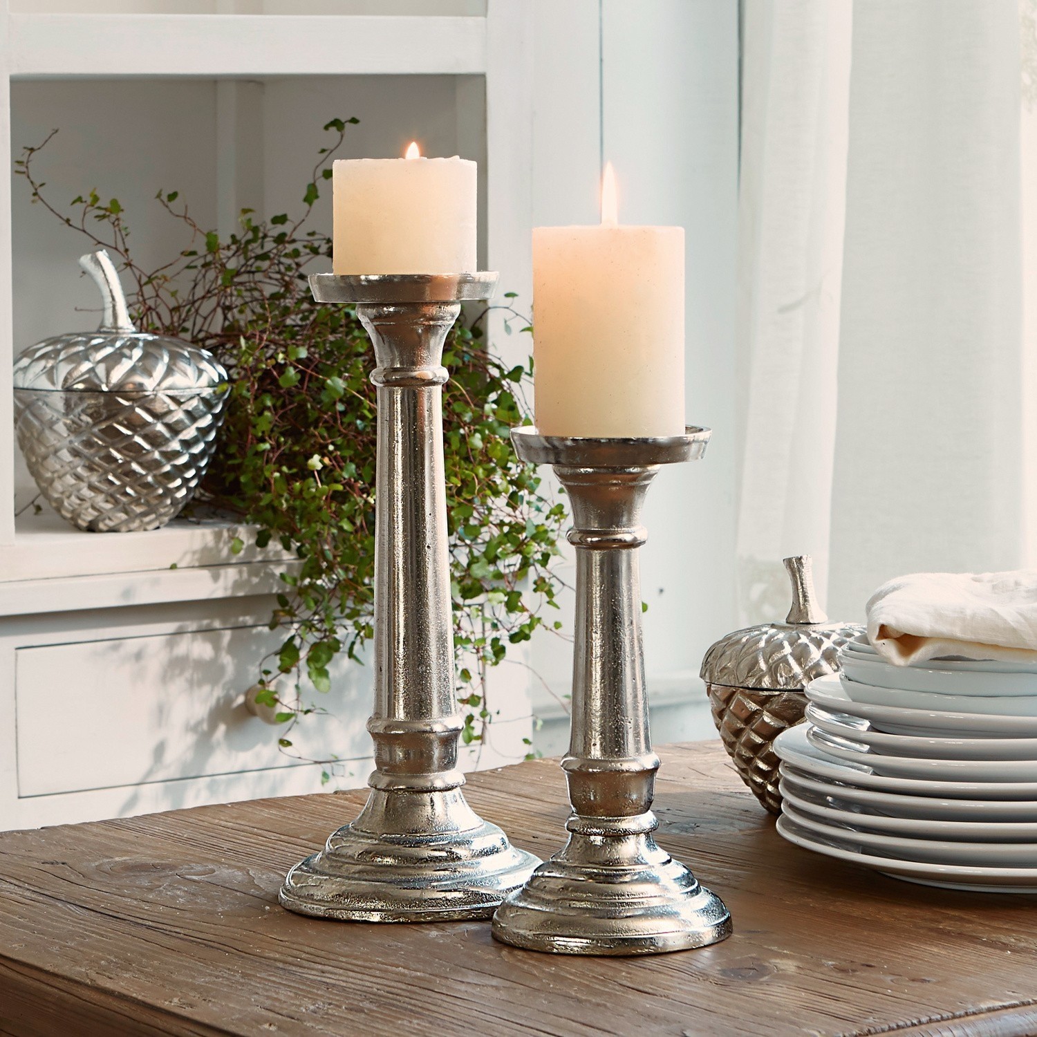 Kerzenständer 2er Set Symone Zwei silberne Metall-Kerzenhalter mit weißen Kerzen auf Holztisch als Wohnaccessoire